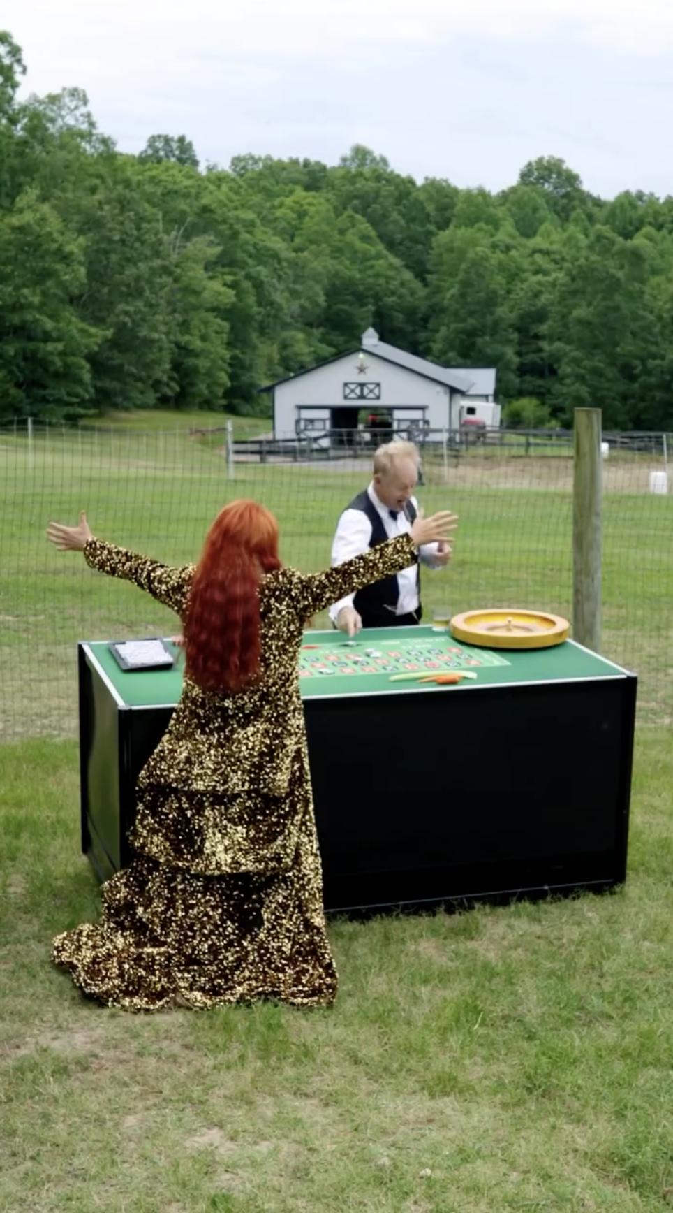 Wearing a gold sequined outfit, Wynonna raises her arms beside an outdoor game table, with a barn and fenced pasture visible behind her. The scene offers a closer look at the open grounds and ranch buildings surrounding her Tennessee home. | Source: Instagram/wynonnajudd