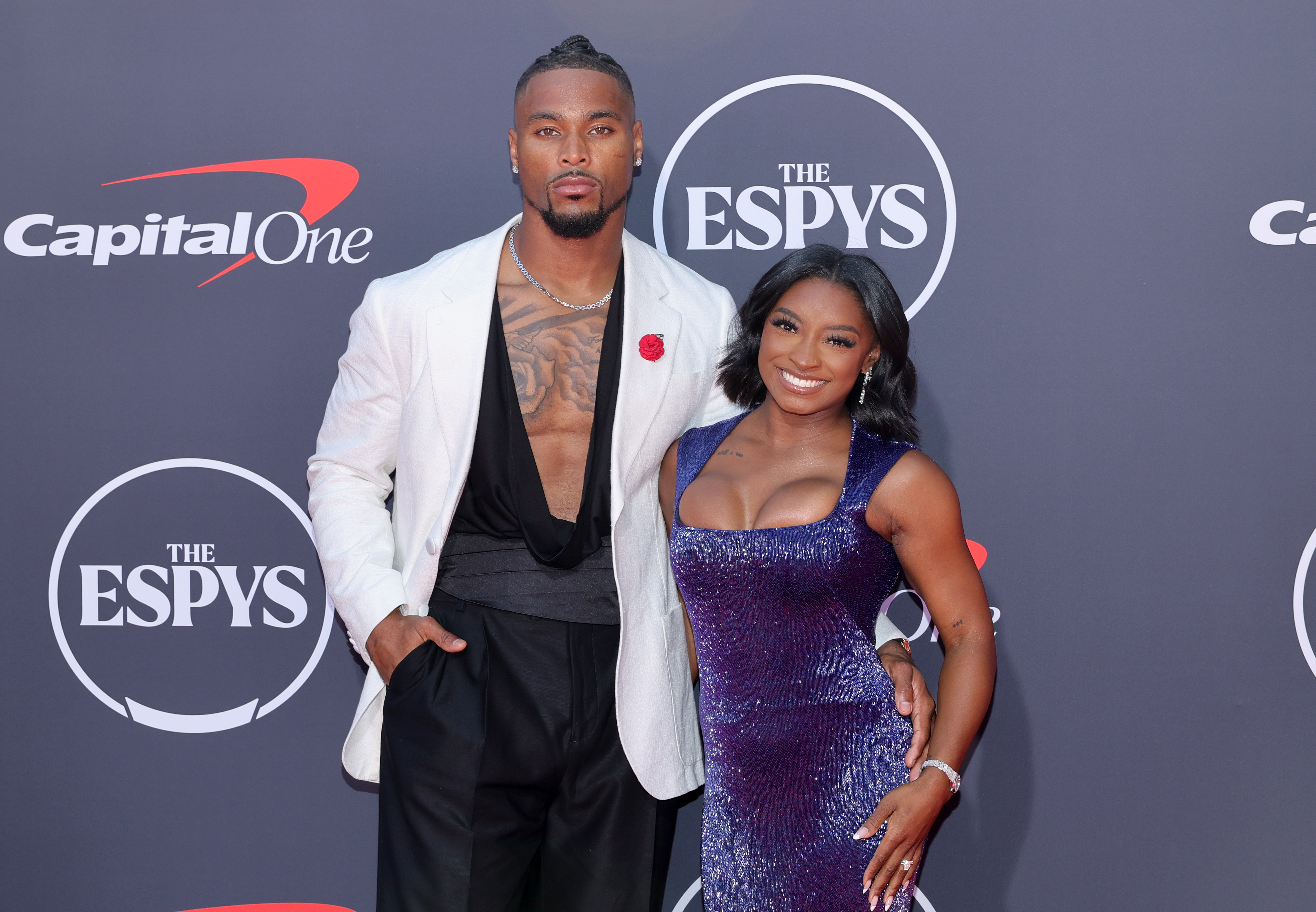 Simone Biles and Jonathan Owens pose arm-in-arm at the 2025 ESPY Awards, flashing confident expressions. Biles beams with a wide smile while Owens maintains a composed, serious look as they stand side by side in their coordinated evening attire.