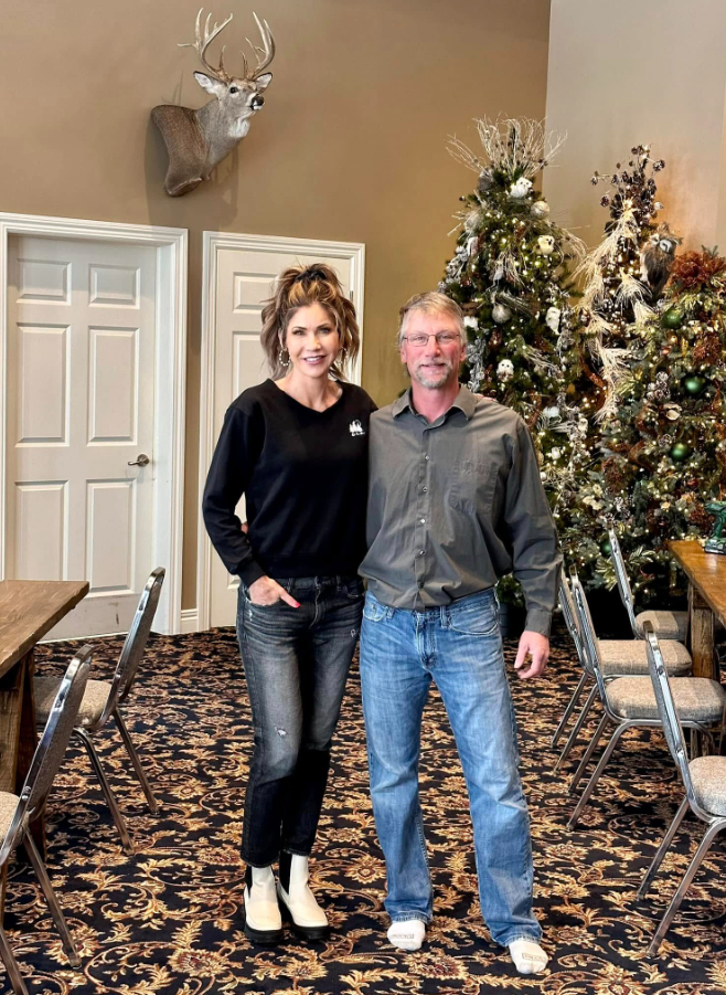 Holiday decorations change the look of the room, with several Christmas trees arranged near the tables and chairs. A deer mount hangs high on the wall above the white doors. | Source: Facebook/kristi.noem