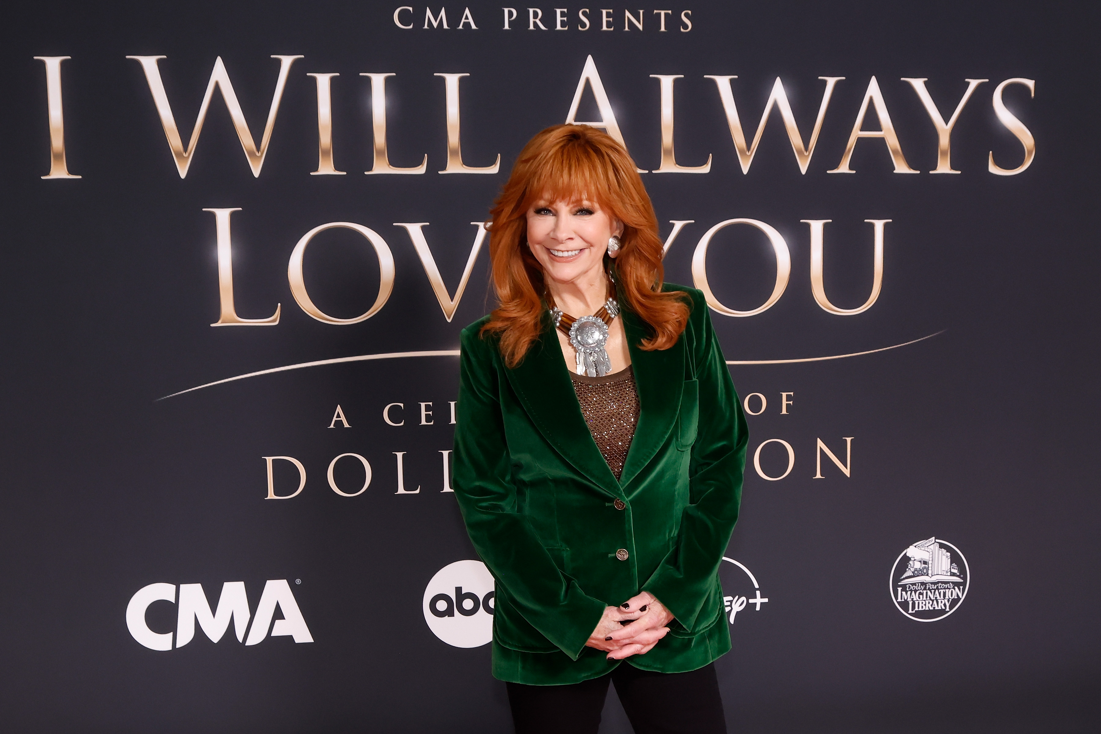 Reba McEntire attends "CMA Presents I Will Always Love You: A Celebration of Dolly Parton" at The Fisher Center for the Performing Arts in Nashville, Tennessee, on October 21, 2026. The country icon smiles on the red carpet in a tailored emerald-green velvet blazer worn over a shimmering bronze scoop-neck top and dark pants, accessorized with a bold Native American turquoise-and-silver squash blossom necklace. | Source: Getty Images