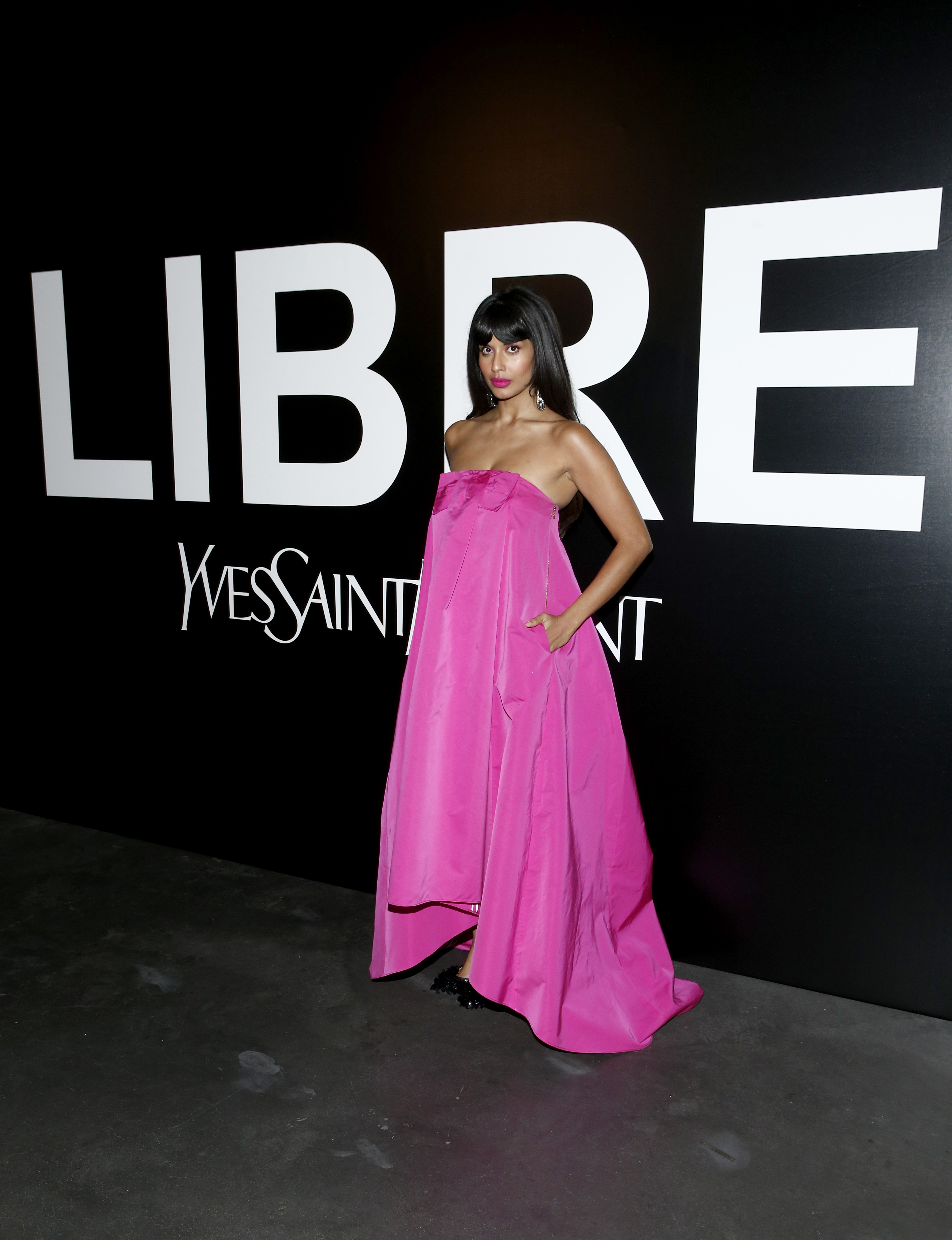 Jameela Jamil poses in a bright pink strapless gown against the Libre backdrop at the YSL Beauty launch event in New York City on September 9, 2019 | Source: Getty Images