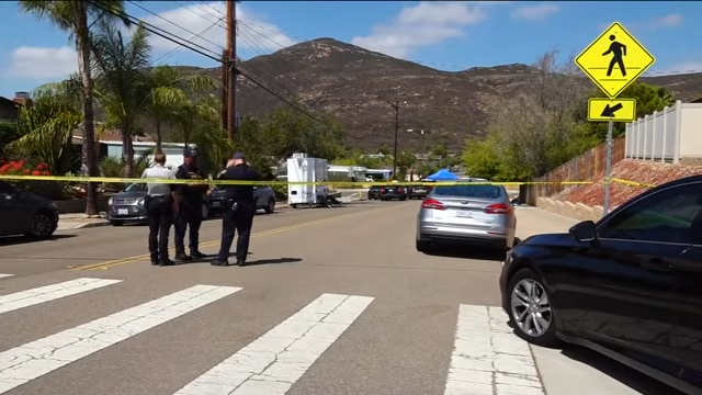 Police officers stand behind crime scene tape on a residential street in San Carlos as authorities investigate the deaths of Amy, David, and Mya Voight. | Source: YouTube/FOX 5 San Diego
