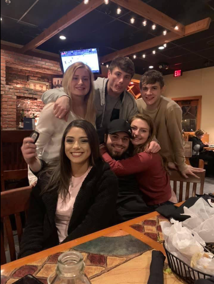 Jack Pugh leans into a crowded restaurant table, surrounded by friends pressed close in laughter and warmth. | Source: Facebook/KennaLynMcClelland