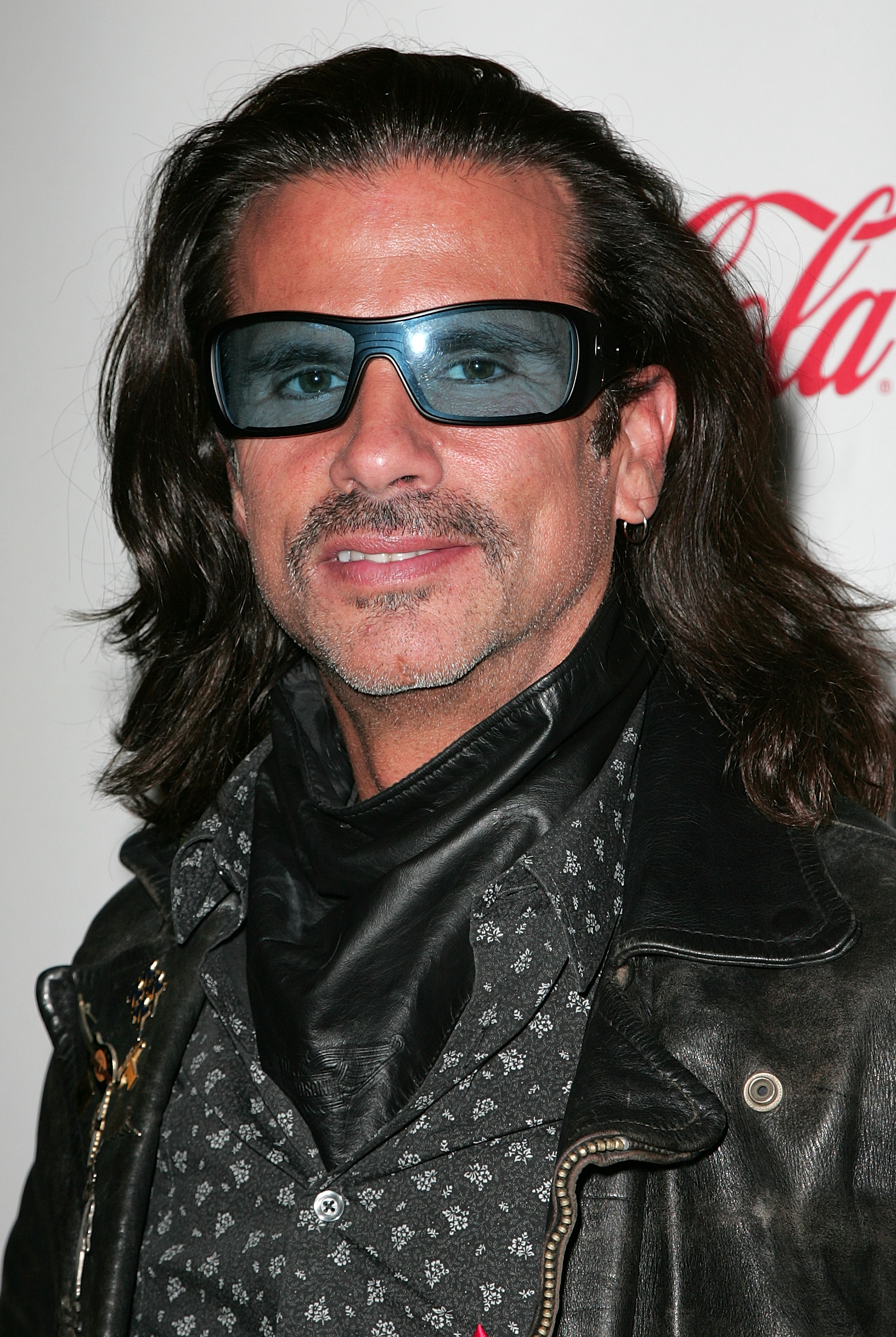 Lorenzo Lamas brings heavy biker edge to the 2009 Hollywood Christmas Parade at The Roosevelt Hotel in Hollywood, California, on November 29, 2009. Smiling subtly with trimmed facial hair, the actor accessorizes his signature shoulder-length dark mane with blue-tinted wraparound sunglasses, a dark leather neck gaiter, a patterned button-down, and a weathered leather jacket. | Source: Getty Images