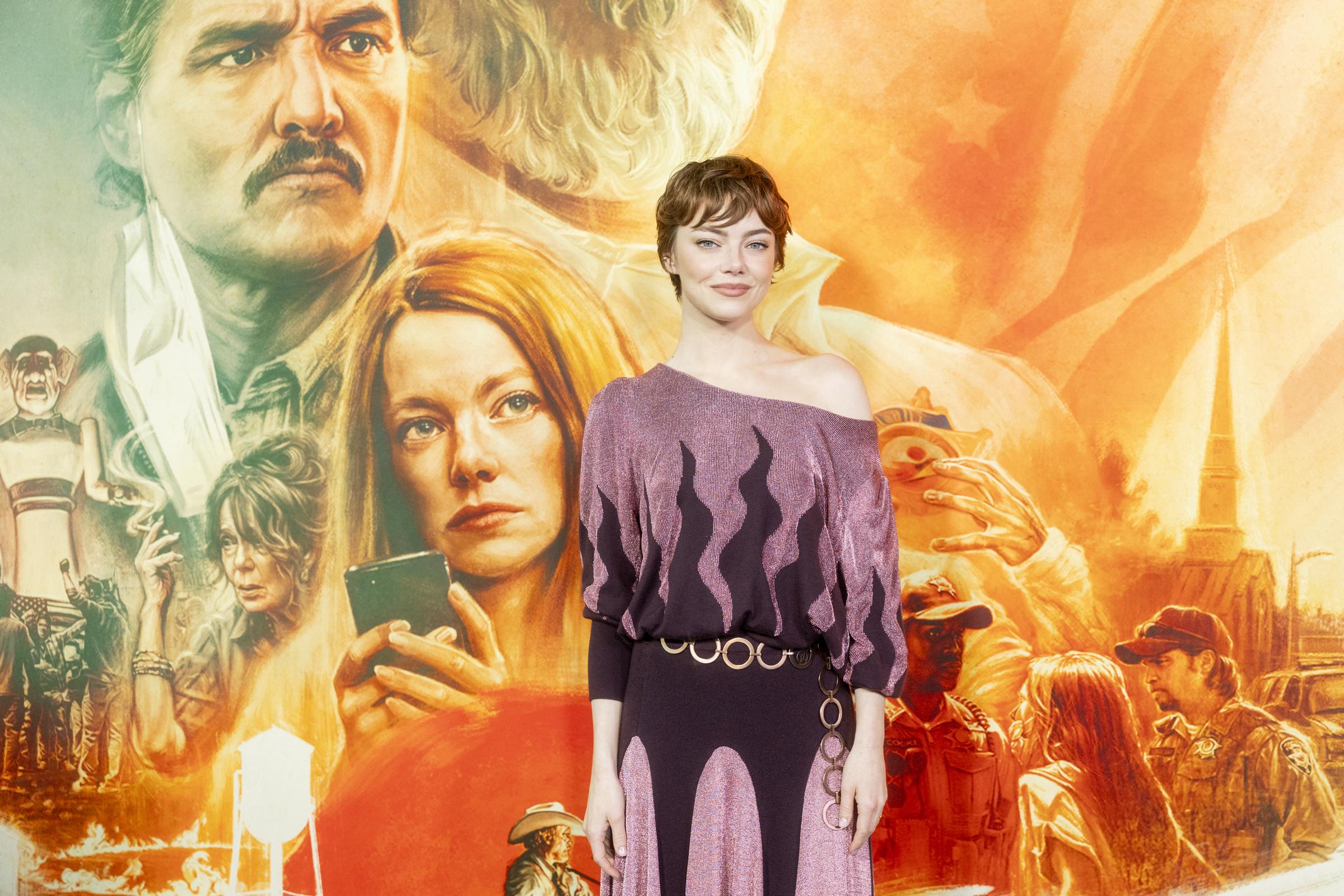 With a serene confidence, Stone meets the camera's gaze with a gentle smile, her poised presence powerfully showcased against the expansive and vibrant promotional artwork of the film, where her own likeness and Pedro Pascal's can be clearly seen.