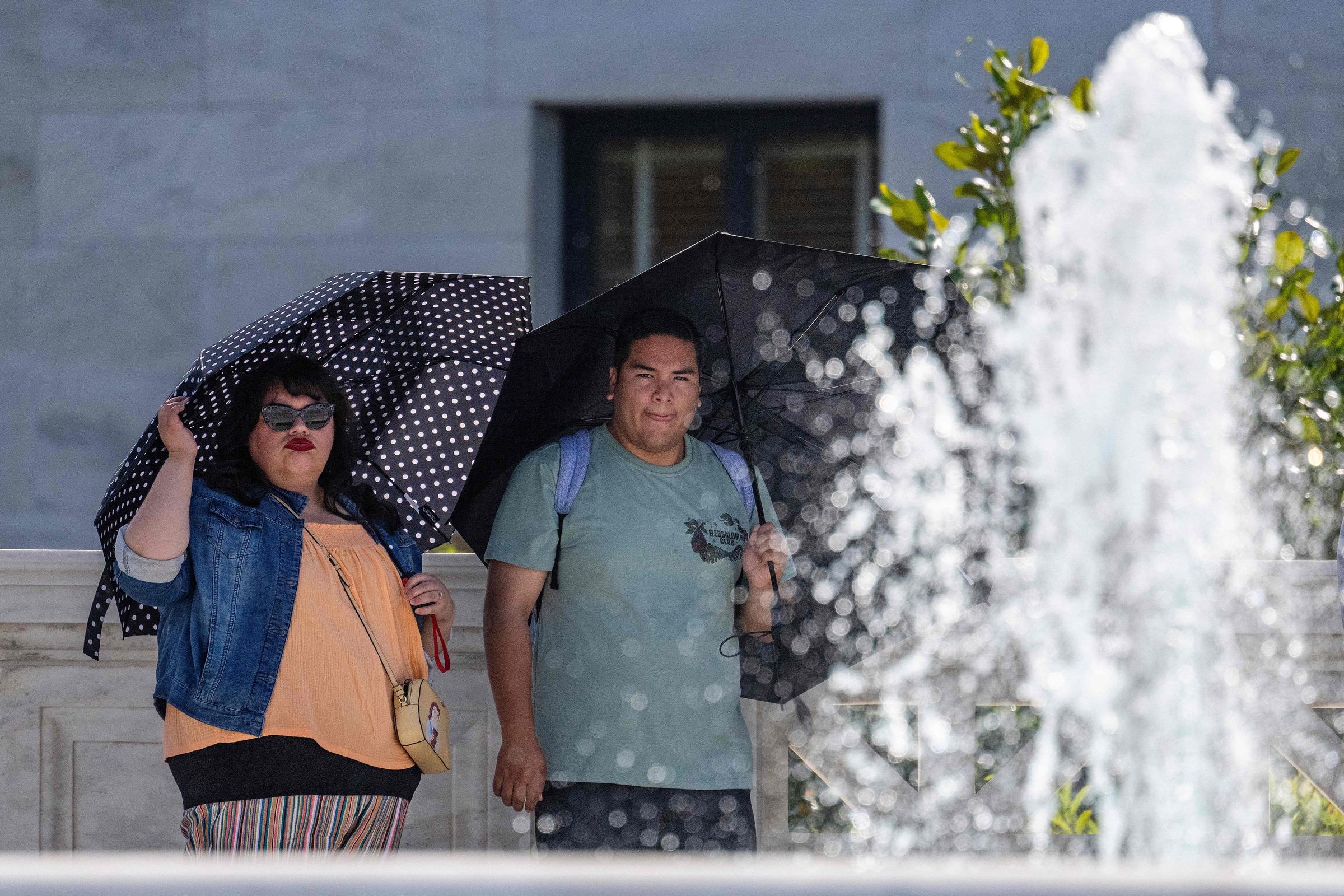 Tourists shield themselves with umbrellas near a fountain in Washington, D.C., as a heatwave settles over the area on June 26, 2023 | Source: Getty Images