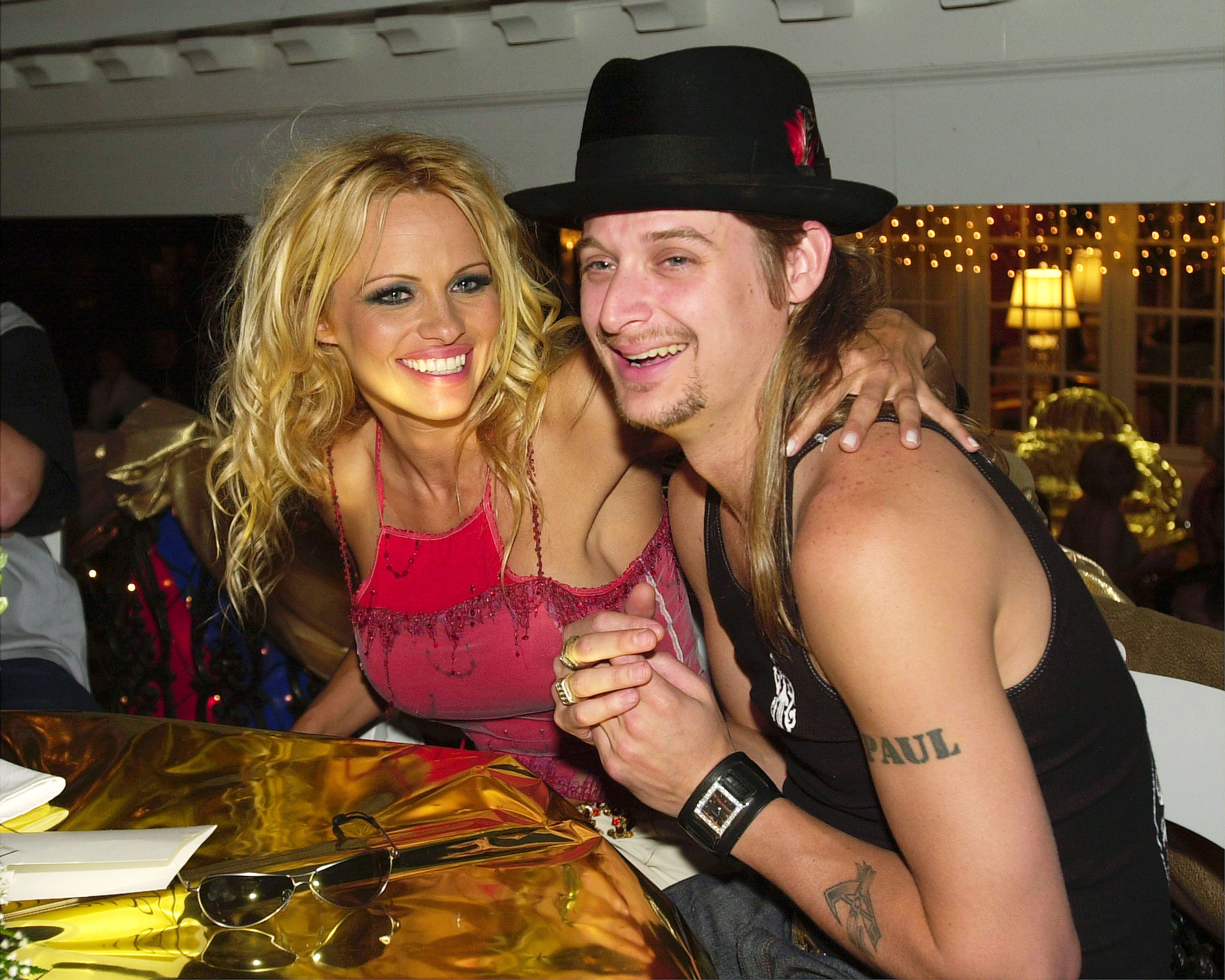 Pamela Anderson and musician Kid Rock share a laugh as they settle into their seats at the Barnstable-Brown Derby Eve Gala in Louisville, Kentucky, on May 4, 2001. Dressed in an embroidered magenta top with sunglasses resting on the gold-covered table, Anderson wraps an arm around Rock, capturing the high-energy celebrity spotlight of her early 2000s relationships before trading red carpet spectacles for the quiet solace of Arcady. | Source: Getty Images