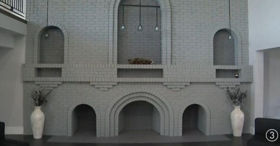 A large brick feature inside Mike Tyson's former home took on a dramatically lighter appearance during the conversion, with its masonry painted in soft gray tones and decorative white vases positioned on either side. Arched recesses remained incorporated into the structure, preserving its unusual shape while the surrounding room adopted the restrained furnishings and neutral palette introduced throughout the church's renovated interior spaces. | Source: YouTube/WKYC Channel 3