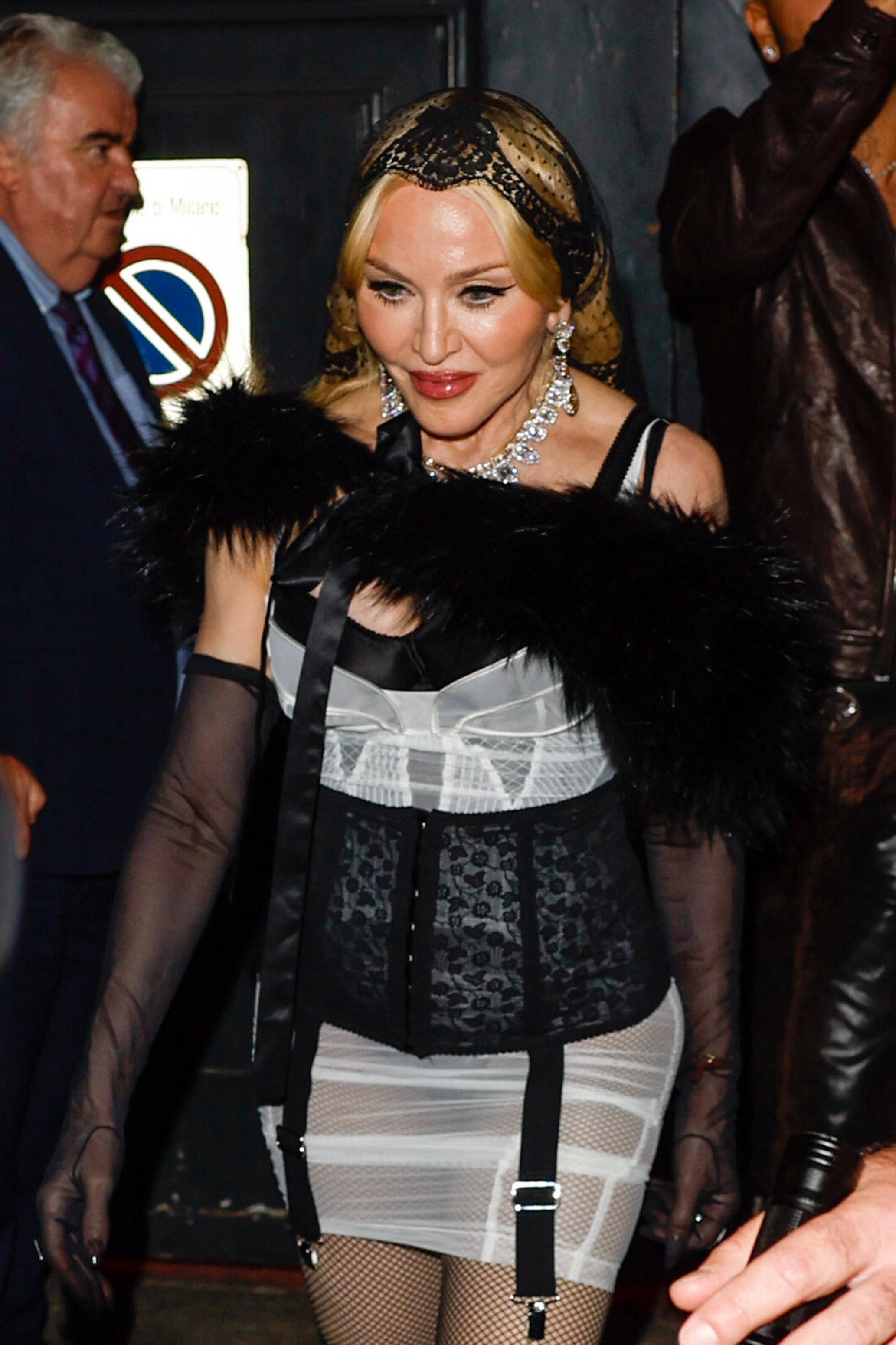 Madonna leaves a Dolce & Gabbana after-party in Milan on September 21, 2024. She stepped out in a black-and-white ensemble with sheer gloves, feathered detailing, jeweled accessories, and a black lace head covering. | Source: Getty Images