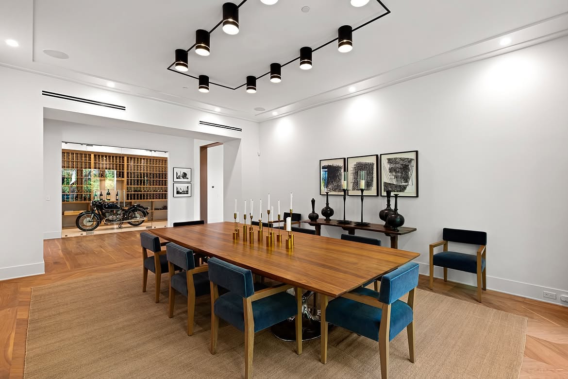 From this angle, the dining room's connection to the wine display becomes even clearer. The long wood table and blue chairs occupy the foreground, while the motorcycle and rows of bottles create an unexpected backdrop. | Source: Instagram/tomer.fridman