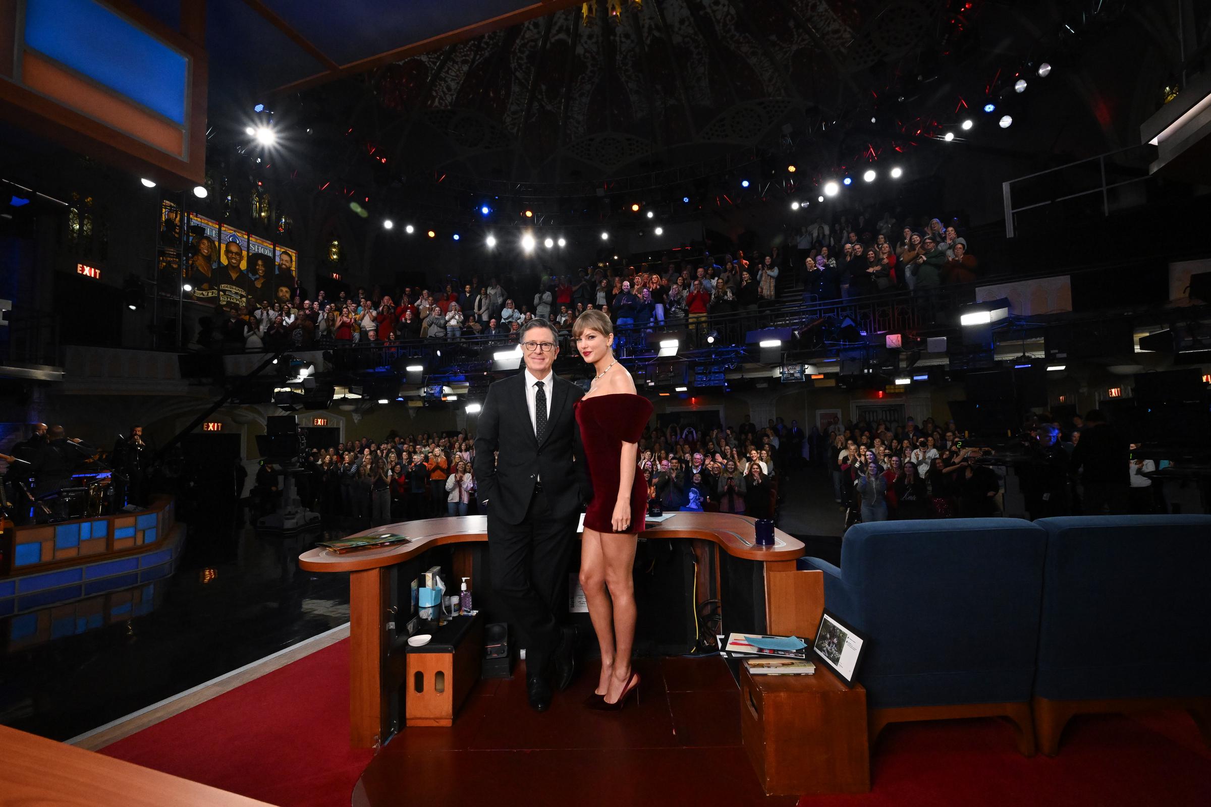 Taylor Swift joins Stephen Colbert at center stage for a photo-op as the audience erupts in applause. The singer’s leggy, high-glam look stood out beneath the studio lights, creating buzz both in the studio and across social media platforms.