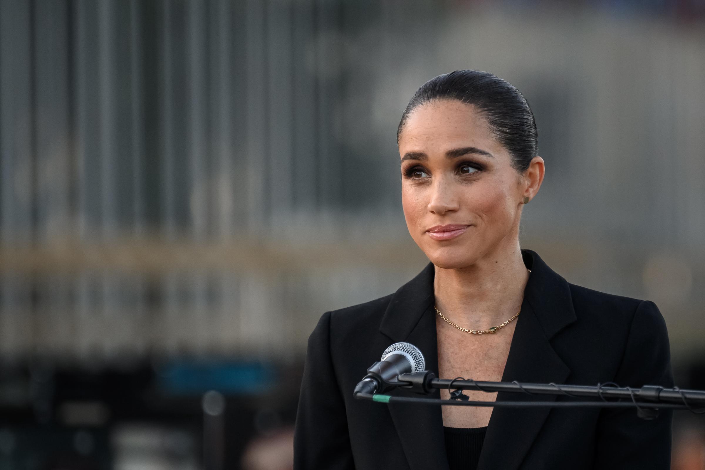 Meghan spoke at a public event in May 2026, wearing a black blazer and gold necklace as she stood behind a microphone. | Source: Getty Images