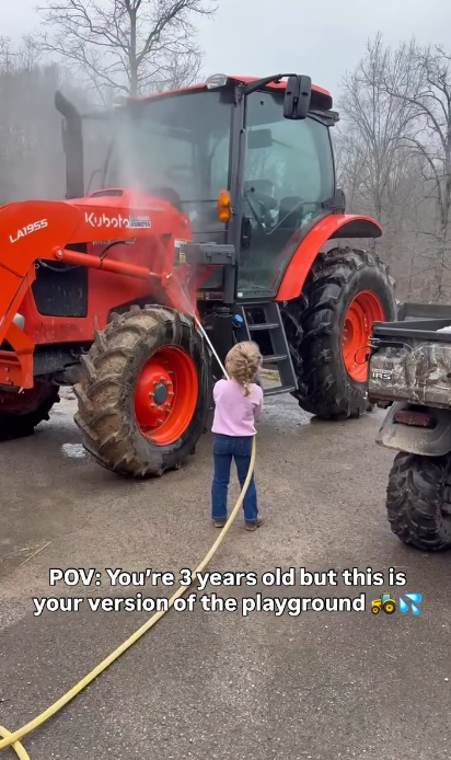 Kaliyah stands beside a large tractor, holding a hose as water sprays across the vehicle. The video describes the activity as her version of a playground at age 3, offering a glimpse of the farm experiences she enjoyed before turning 4. | Source: Instagram/wynonnajudd