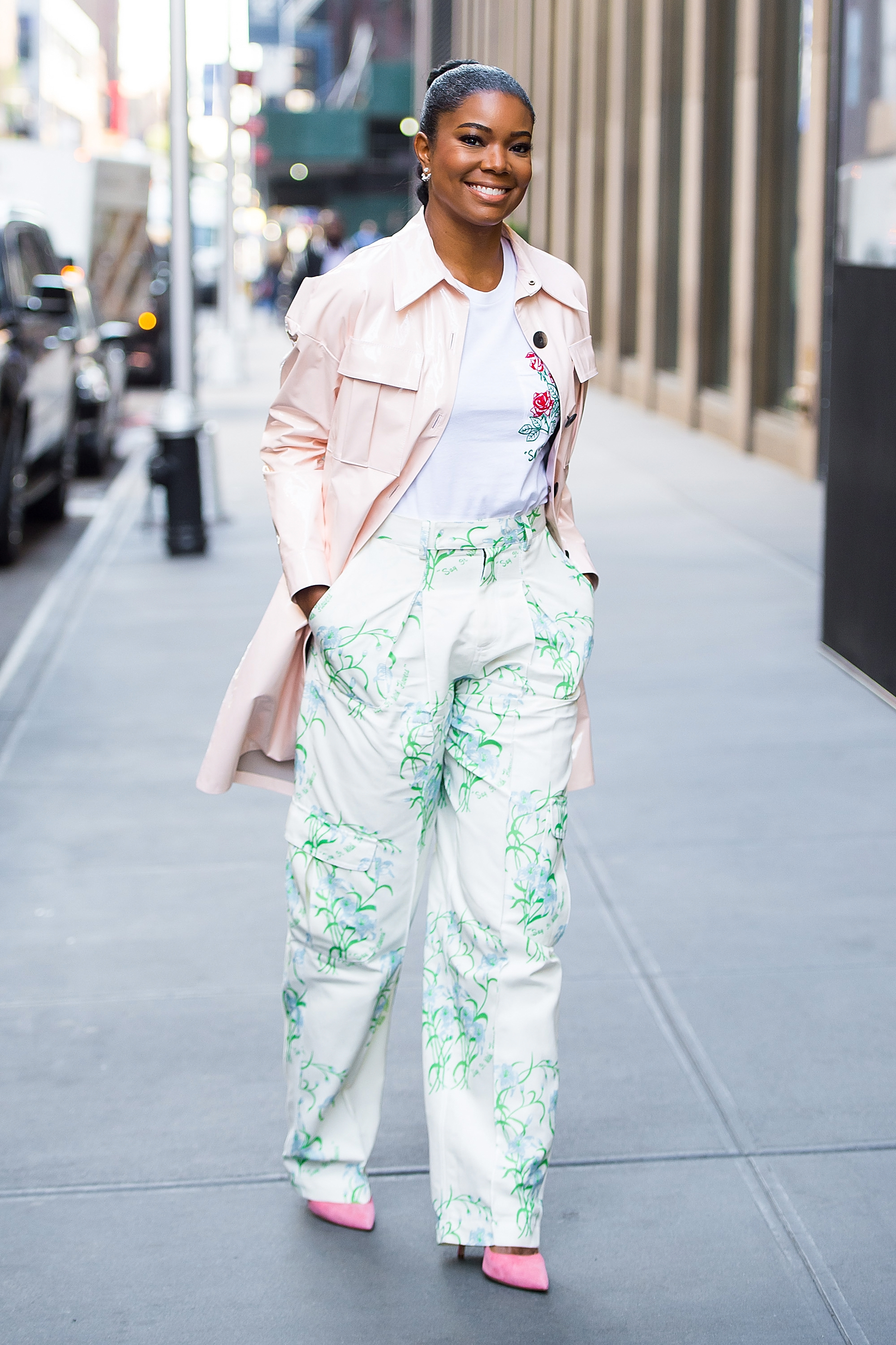 Gabrielle Union walks confidently down a city sidewalk, hands in her pockets. She wears a pale pink jacket over a white top and high-waisted, loose-fitting pants with a green floral pattern, paired with pink heels. | Source: Getty Images