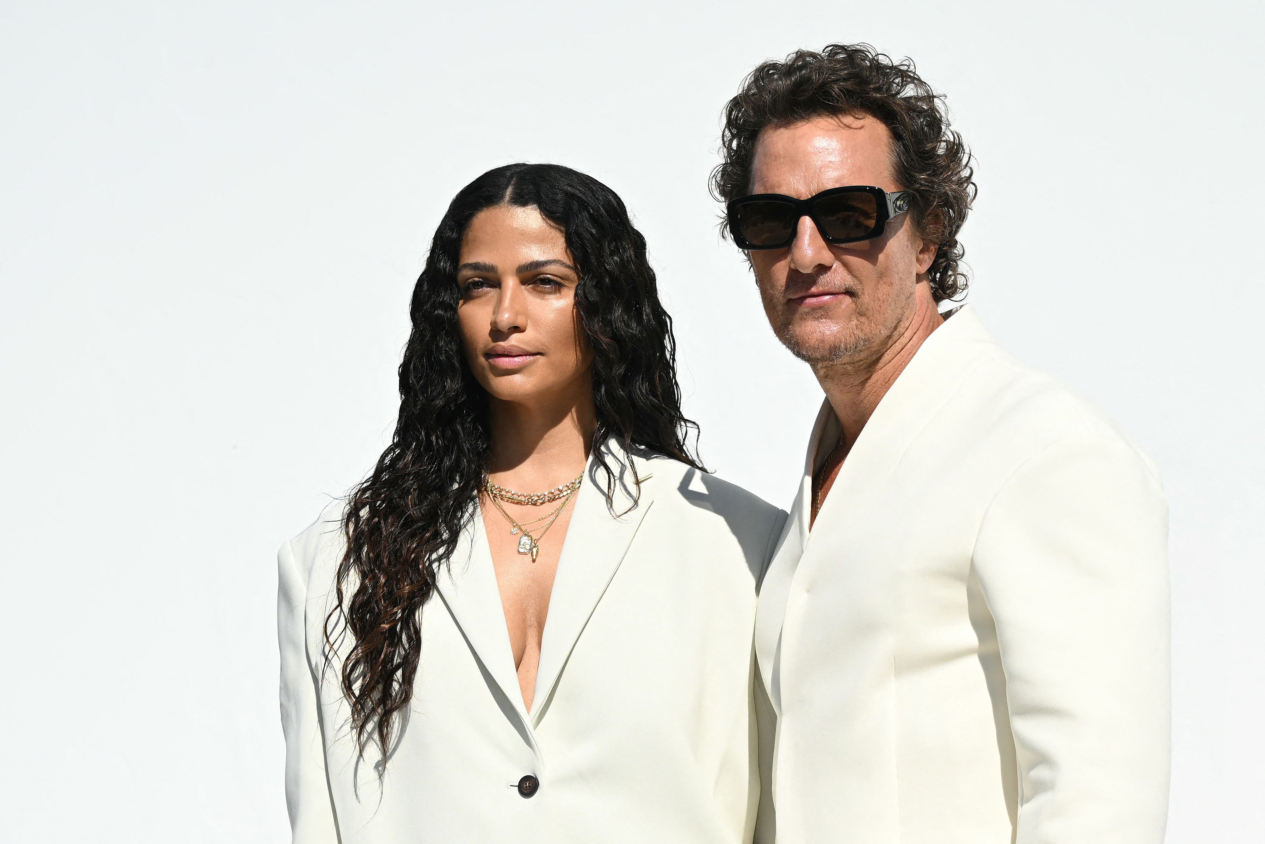 Alves poses next to McConaughey in a close-up shot that showcases her accessories in detail. A silver combined double pendant necklace hangs elegantly around her neck, adding a delicate yet striking accent to her tailored cream ensemble.