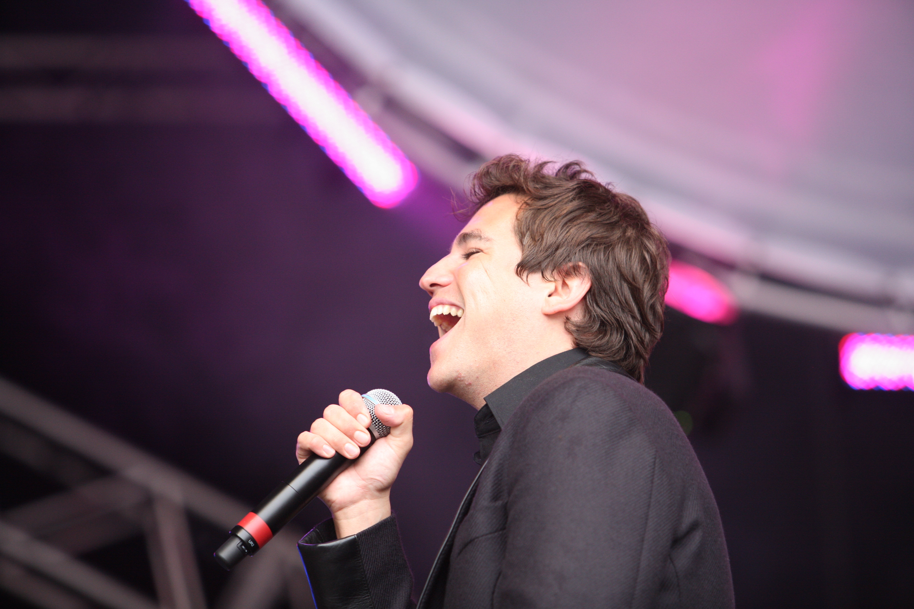 The singer performs live onstage in the United Kingdom, microphone in hand and a look of joy on his face. His expression reveals the depth of emotion as he is fully immersed in the moment.