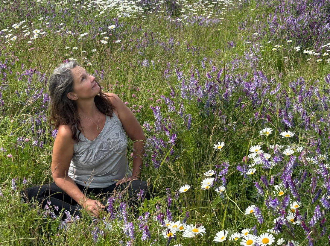 Sitting among purple wildflowers and white daisies in 2026, Judd looks toward the sky with her gray-streaked hair falling loosely around her shoulders. The outdoor setting offers a glimpse of her life away from Hollywood events.