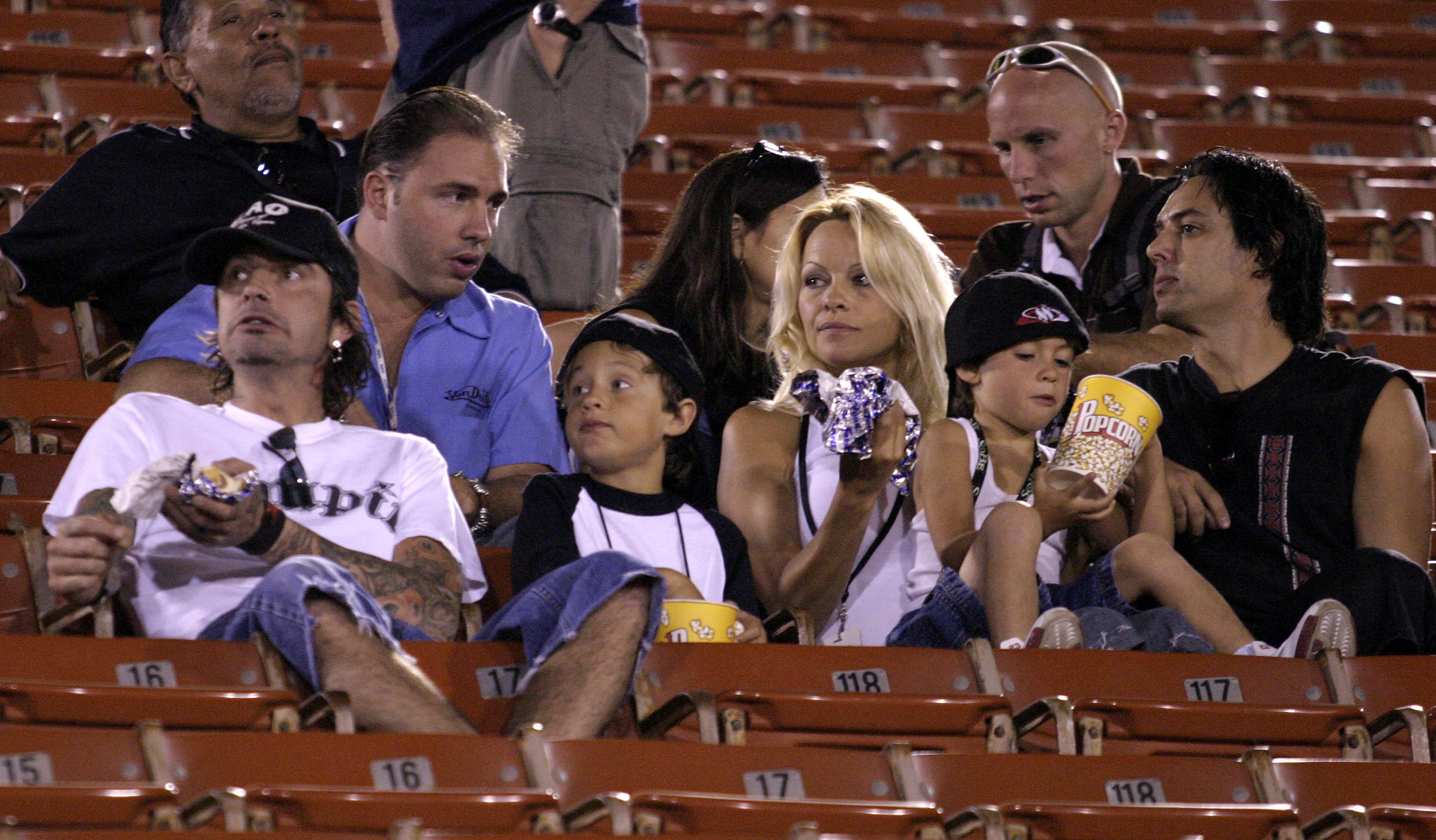 Pamela Anderson and Tommy Lee attend the Moto X Freestyle competition at the X Games with their sons, Brandon Thomas and Dylan Jagger, at the Los Angeles Memorial Coliseum. Seated in the stadium's orange bleachers, the family shares snacks while watching the event, with both boys dressed in matching black and white outfits.