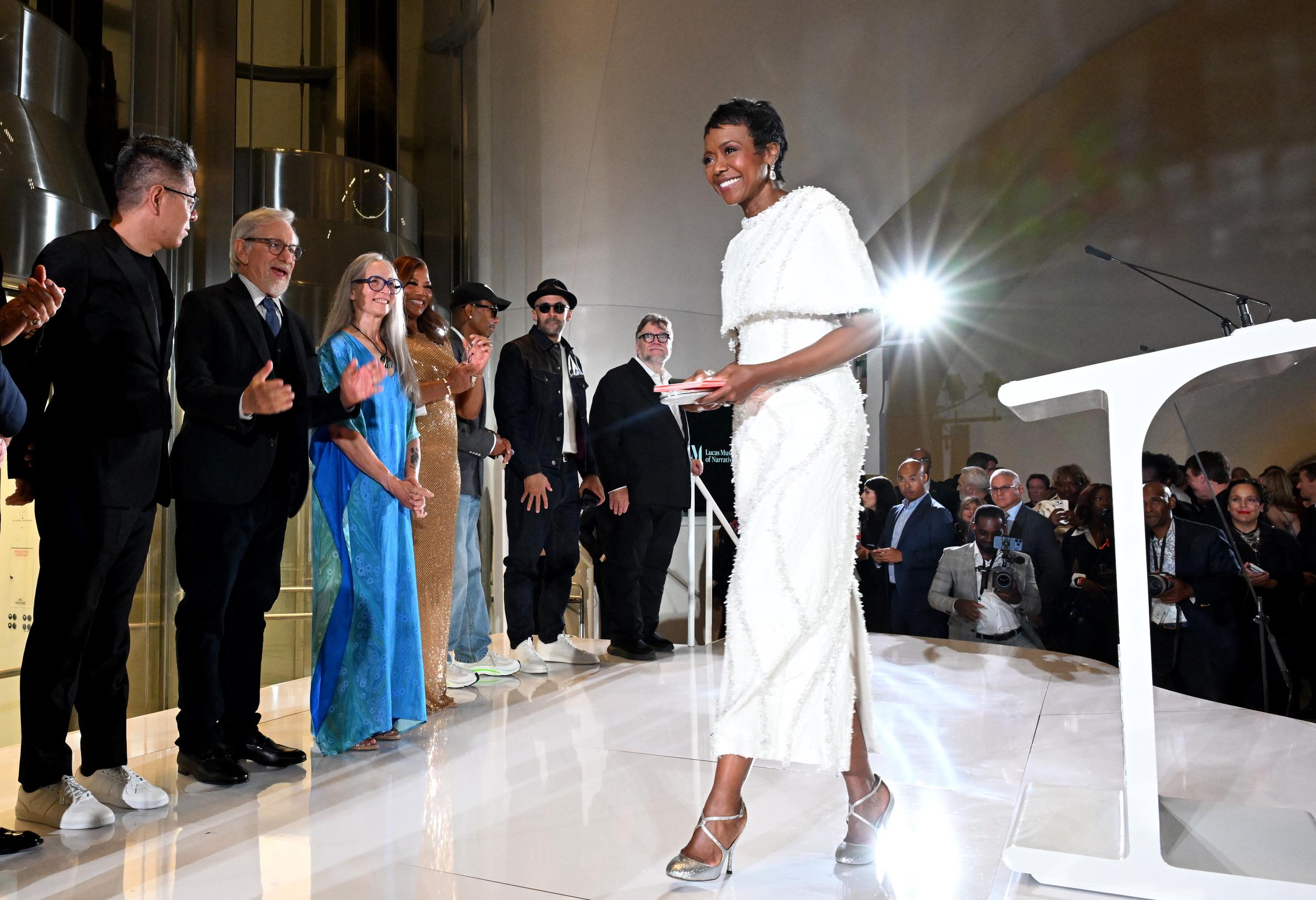 Mellody Hobson stepped forward during the opening-night program as guests applauded behind her. Ma Yansong, Steven Spielberg, Julie Bell, Queen Latifah, Pharrell Williams, JR, and Guillermo del Toro were among those gathered nearby. | Source: Getty Images