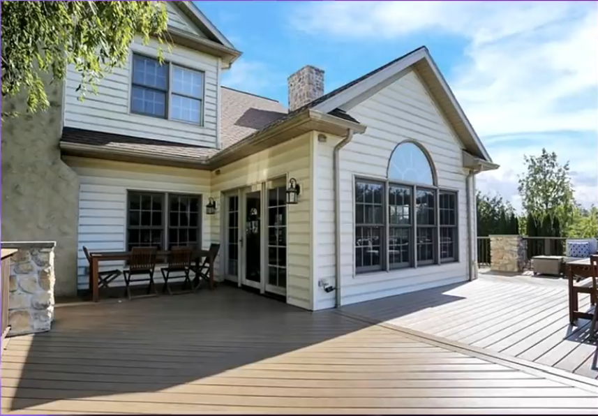 A closer view of the home's rear entrance highlights the white siding, large arched window, and French doors opening onto the broad wooden deck. Outdoor dining and lounge furniture complete the space, showcasing the property's traditional exterior design.