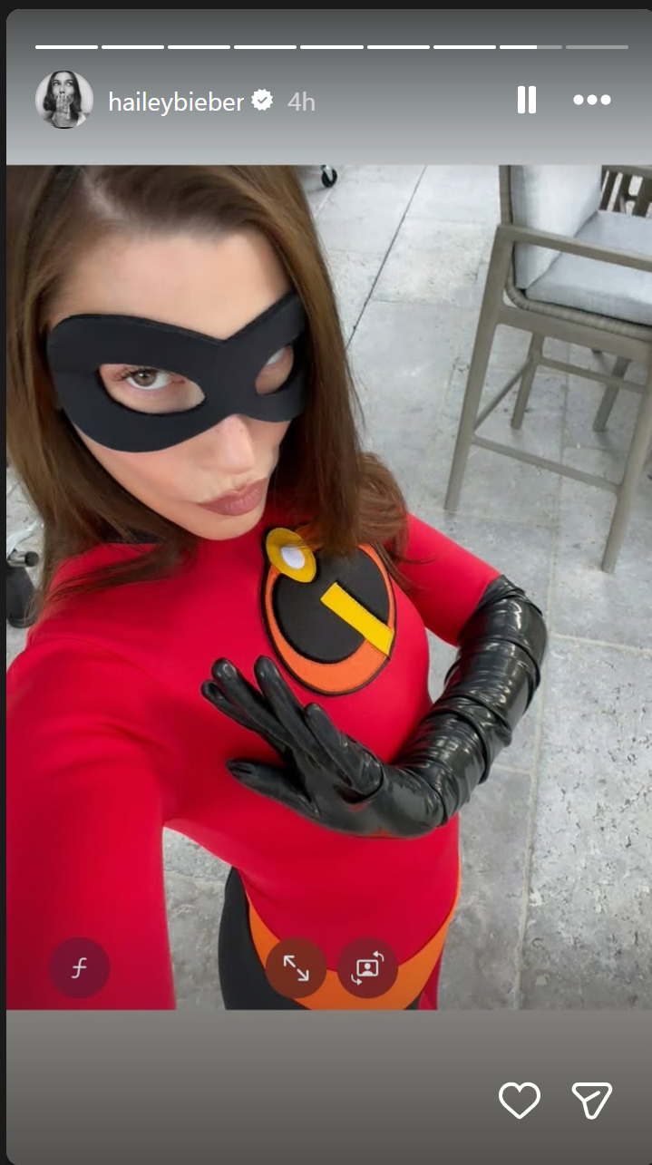 In a November 1 Instagram story, Bieber suited up as Elastigirl from "The Incredibles," showing off a sleek, form-fitting red bodysuit with the iconic "i" emblem across the chest. She paired the look with glossy black gloves, an orange belt, and a matching eye mask. With her hair styled down and a perfectly arched brow, she nailed the animated heroine's confident flair — equal parts playful and polished. | Source: Instagram/haileybieber