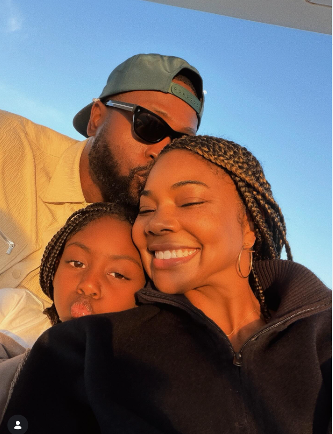 This warm, golden-hour selfie shows Gabrielle Union smiling with her eyes closed as Dwyane Wade leans in from behind to kiss her head, while their daughter Kaavia James Union Wade nestles in front, playfully puckering her lips. | Source: Instagram/gabunion