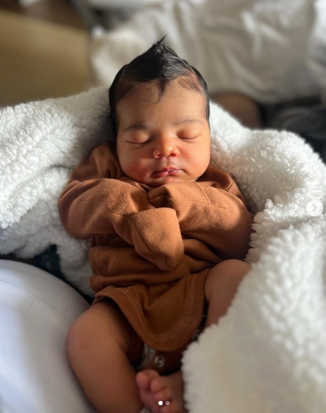 A sleeping Tyreek Jr. is pictured nestled in a soft white blanket while wearing a brown long-sleeved outfit, with his hands tucked beneath his chin. The close-up offered an early glimpse of Tyreek Hill and Camille Valmon's son, who was born on March 12, 2023. The image appeared in a post dated August 14, 2023. | Source: Instagram/tyreekhilljr_