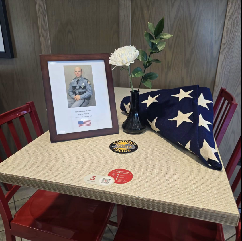 A Chick-fil-A location off Nashville/Campbell Lane honored fallen Kentucky State Trooper Hayden Phillips, Unit 369, with a framed portrait, flowers, and a folded American flag following his death in the line of duty. | Source: Facebook/Sheriff Deputies