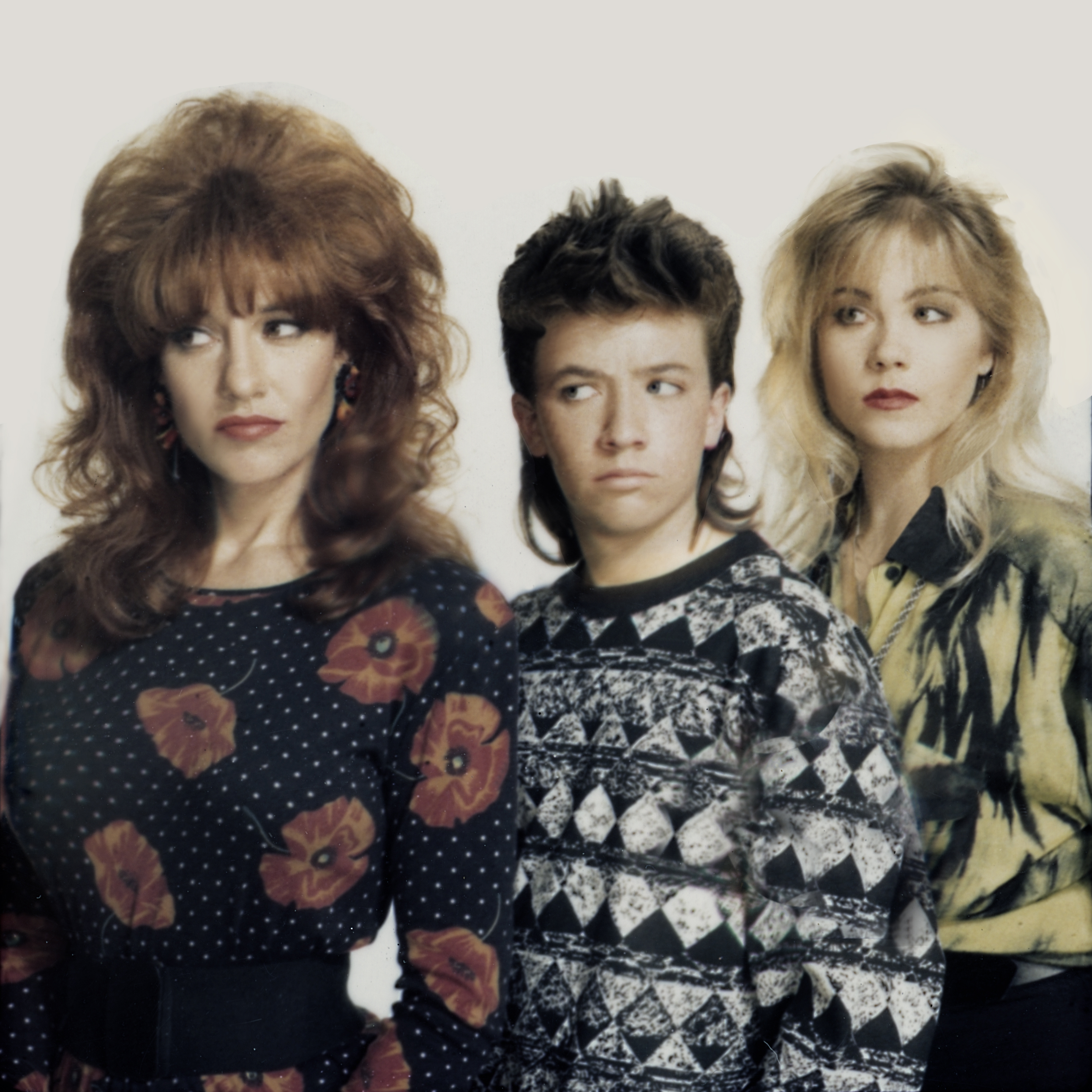Katey Sagal, David Faustino, and Christina Applegate gathered for an early promotional portrait for "Married... with Children" in April 1987 in Los Angeles, California. Flanking Faustino as he cut a deadpan sideways glance, Sagal and Applegate embodied the signature look of Peggy and Kelly Bundy with voluminous teased hair and quintessential 1980s patterned tops during the sitcom's inaugural season. | Source: Getty Images
