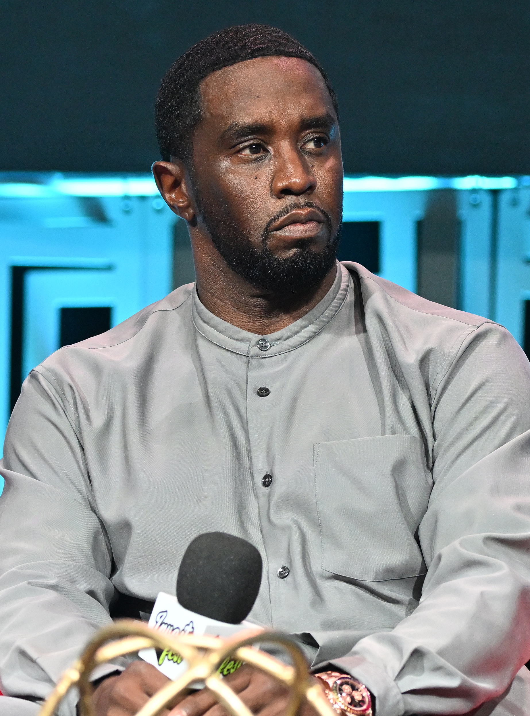 Sean "Diddy" Combs appears focused during a panel at Day 1 of the Revolt Summit x AT&T in Atlanta on August 25, 2023, wearing a gray buttoned shirt with a mandarin collar and a statement watch.