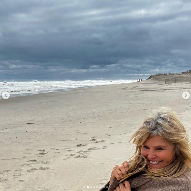 Christie Brinkley's blonde hair reveals hints of gray as she smiles on a windswept beach in March 2023. The model admitted she was still undecided about letting her natural color grow out, despite her son's encouragement. | Source: Instagram/christiebrinkley