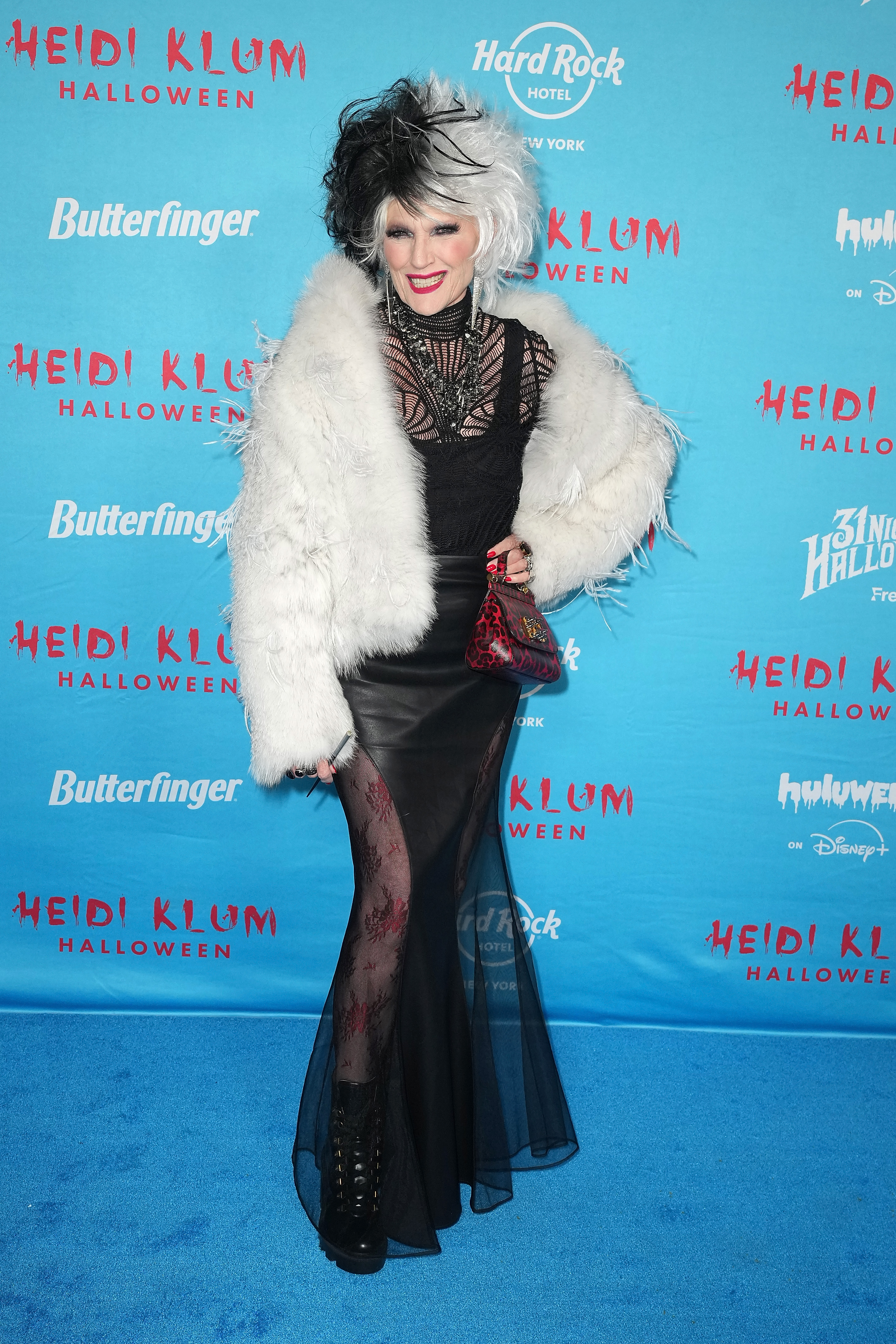 Also at Heidi Klum's 24th Annual Halloween Party, Elon Musk's mother, Maye Musk, embraced full villain mode in a glam Cruella de Vil-inspired look. She wore a voluminous black-and-white wig, a dramatic fur coat style with feathers, and a sheer black gown layered over printed tights. The outfit was finished with lace-up platform boots, a red animal-print handbag, and a statement necklace, delivering high fashion with a mischievous twist.