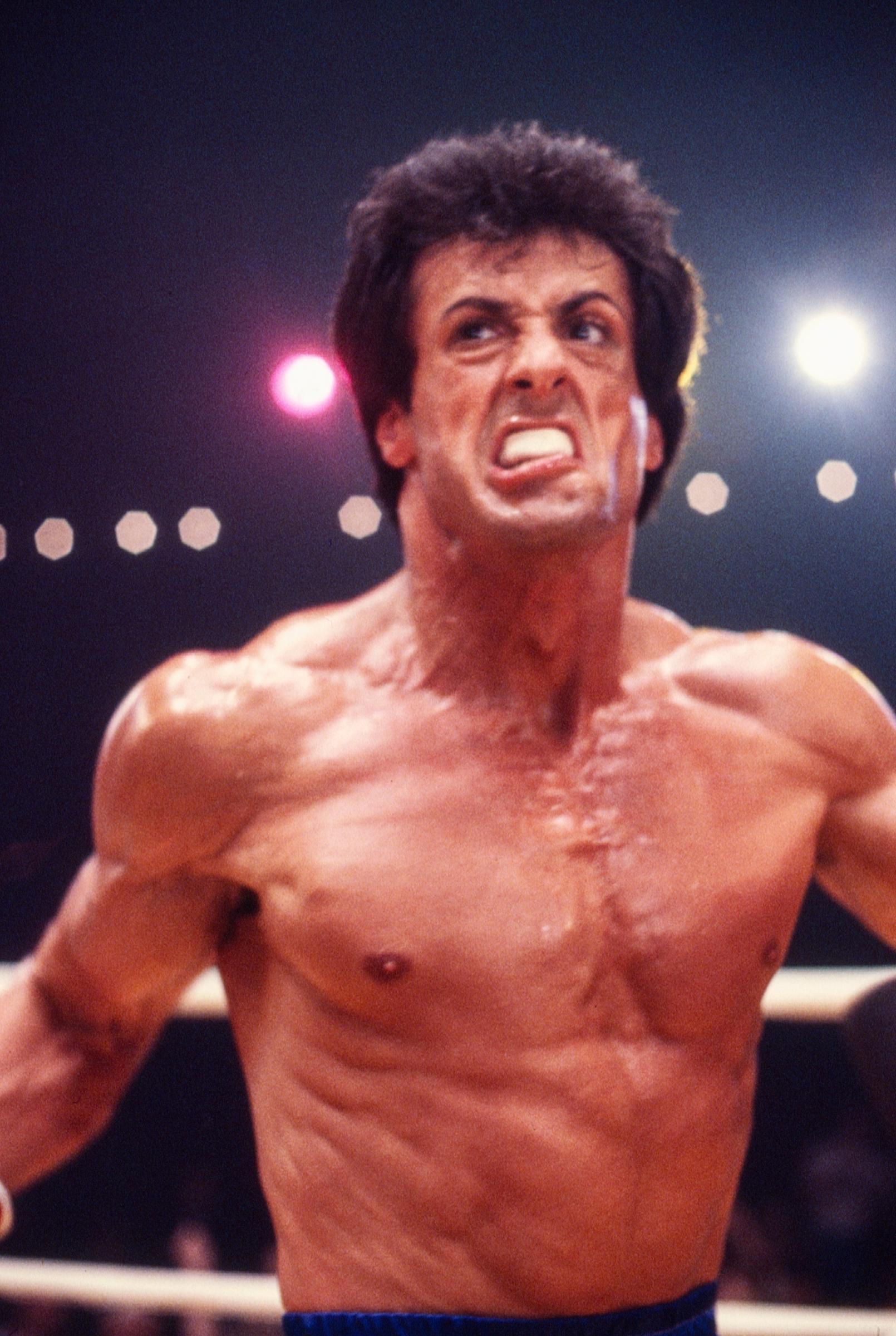 Sylvester Stallone, as Rocky Balboa, throws a staged punch on the boxing set of "Rocky III" in Los Angeles, California, in May 1982. The close-up captures Stallone's exceptionally lean and defined physique, the result of the intense training and restrictive diet he followed while preparing to portray a faster, more agile Rocky.