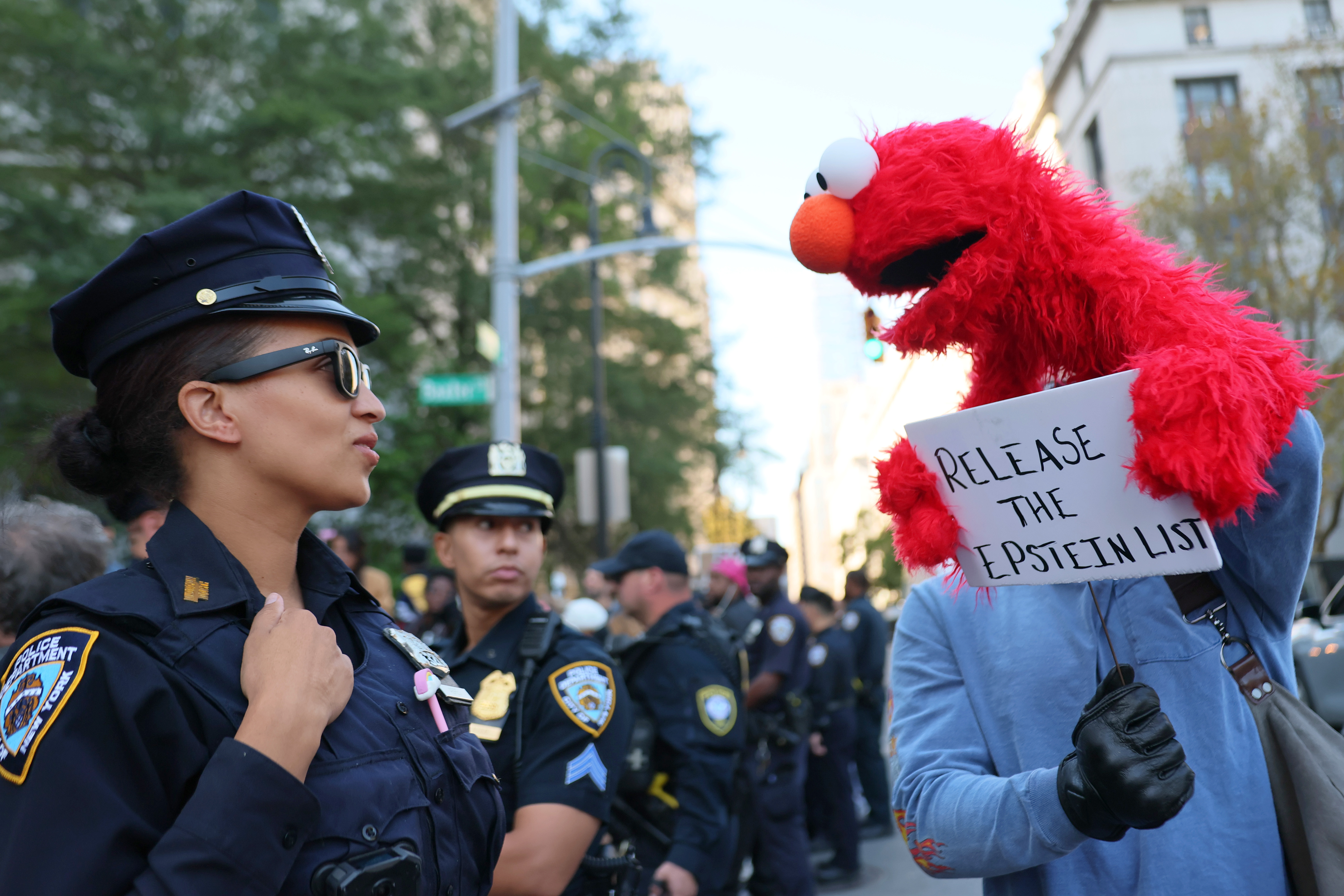 The scene outside the courthouse drew an unusual mix of onlookers, including a protester dressed as Elmo holding a sign demanding the release of the Epstein list while police monitored the crowd. | Source: Getty Images