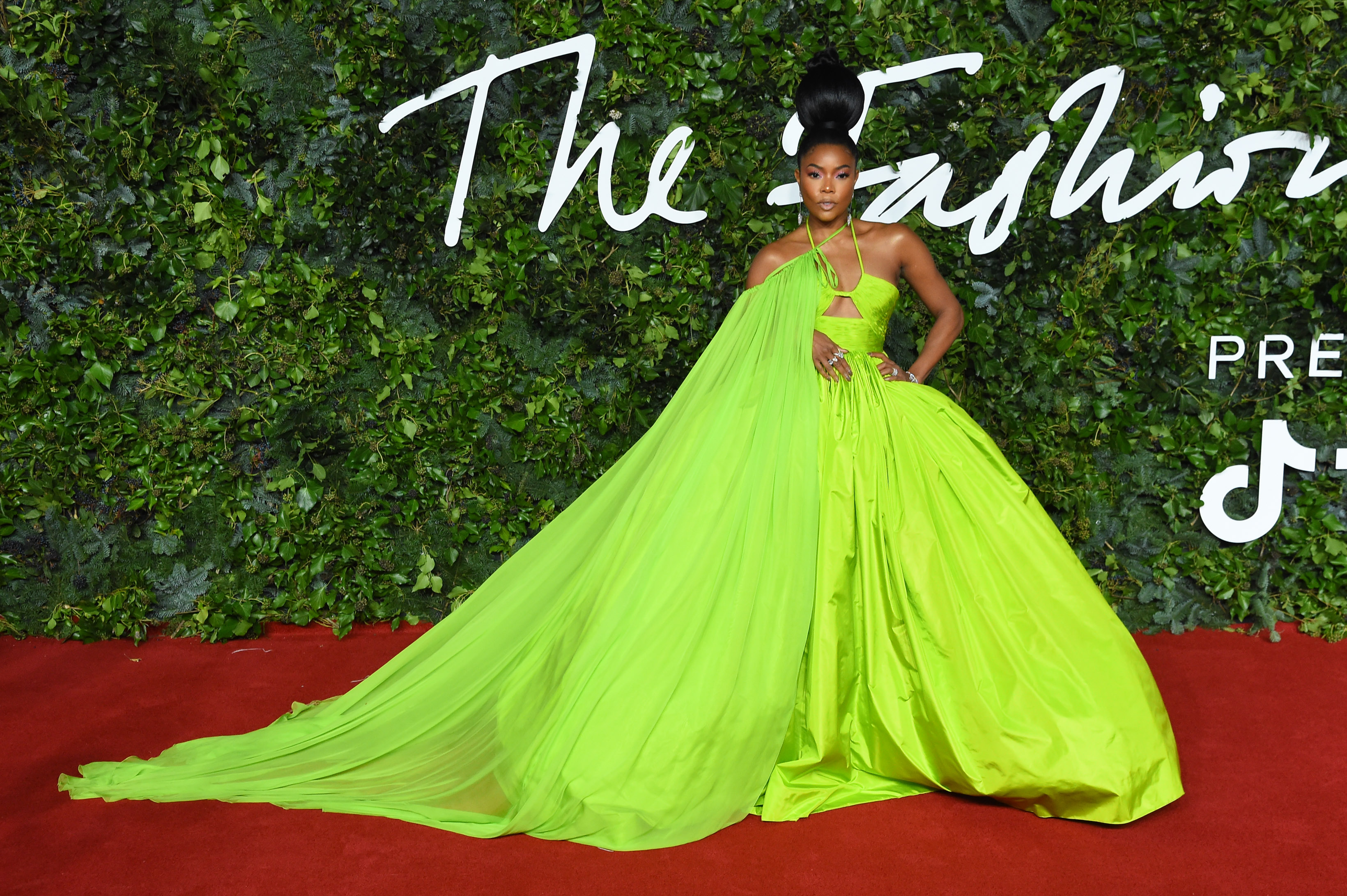 Gabrielle Union poses on a red carpet in a dramatic, flowing neon-green gown with a long train cascading behind her. The dress features a halter neckline and bold cutouts. | Source: Getty Images