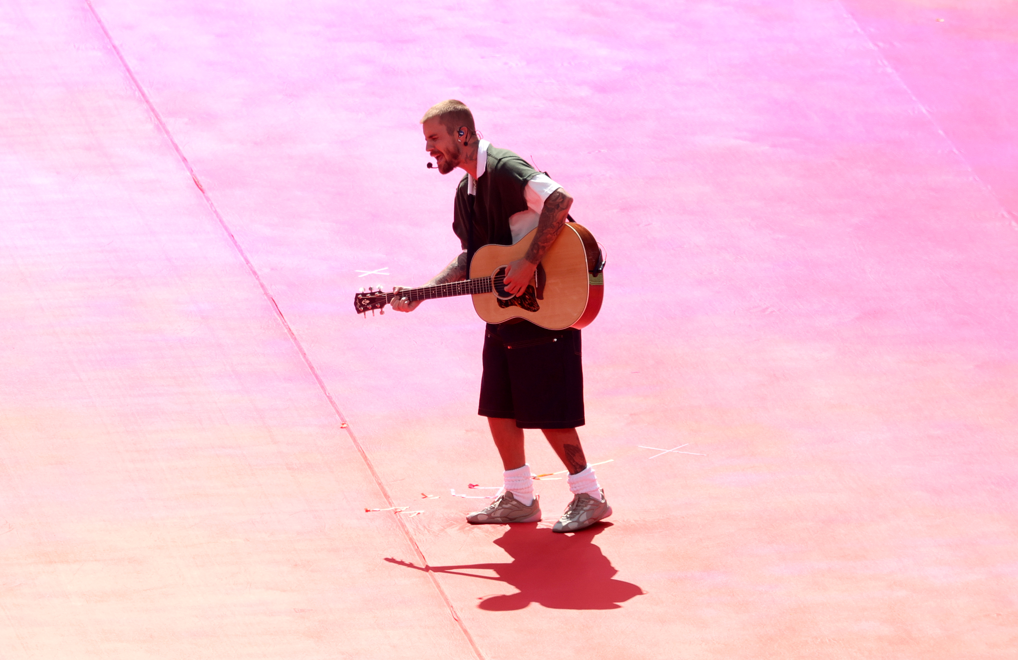 Justin Bieber is captured from a high angle during his Topps Final Halftime Show set, crooning with his guitar against a vibrant, pink-hued stage floor at MetLife Stadium. | Source: Getty Images