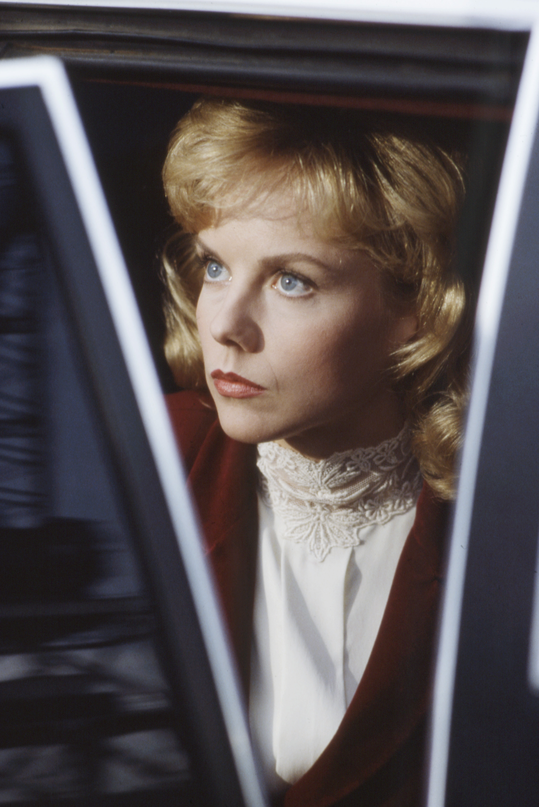 Framed inside a car window, the 30-year-old actress leaned toward a refined, aristocratic intensity for the 1986 TV movie "Dark Mansions" in Mendocino, California. Linda Purl’s side-swept blonde fringe and crimson lips accentuated her sharp gaze, while a Victorian lace high-neck top beneath a rich burgundy jacket underscored a decidedly sophisticated, dramatic turn.