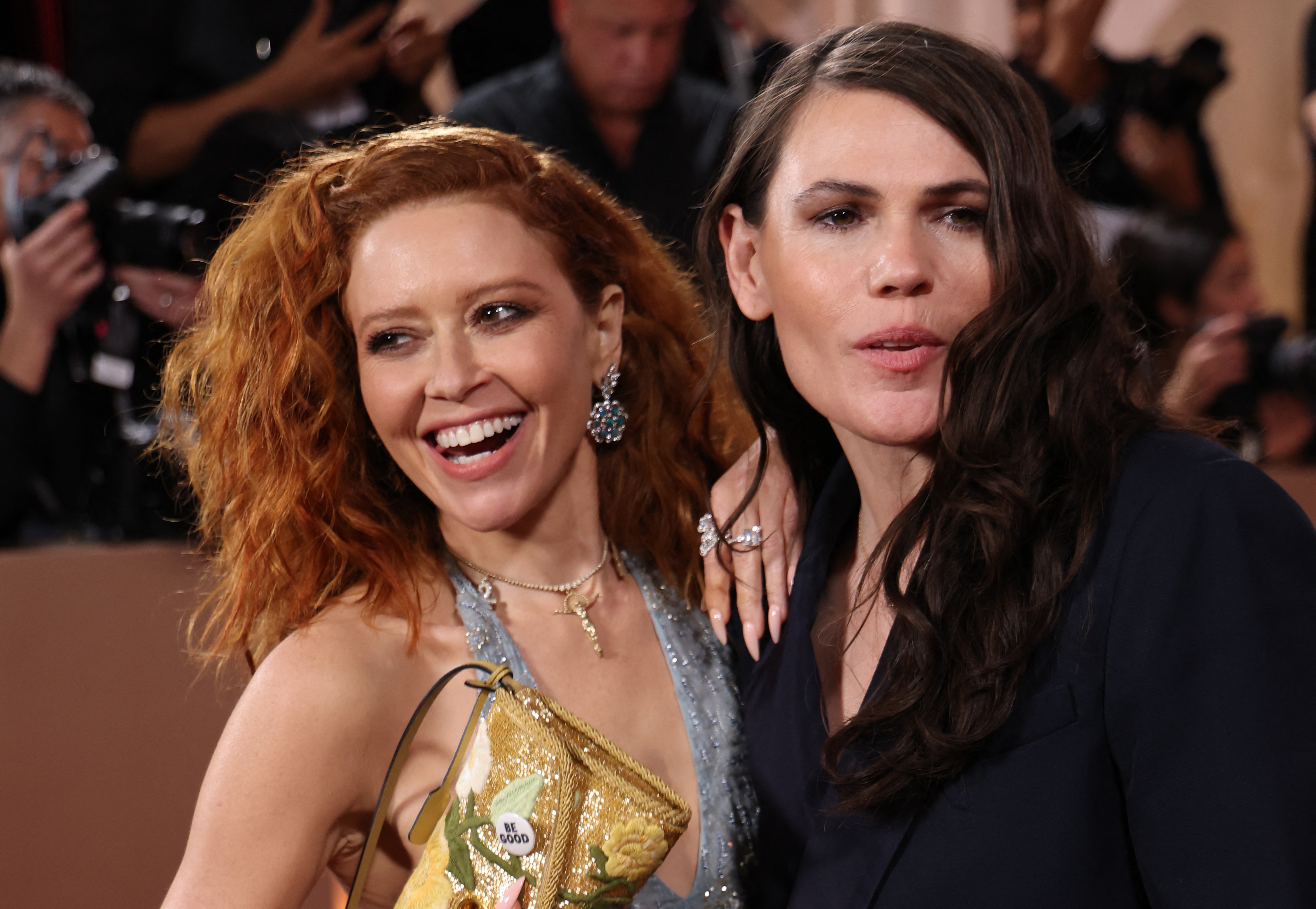 Natasha Lyonne smiling as she holds up her purse with her "Be Good" pin attached to it. She poses next to Clea DuVall at the Golden Globes. | Source: Getty Images