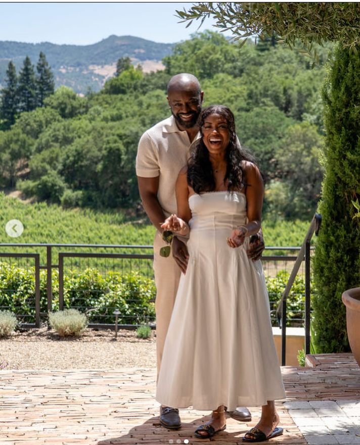 Javicia, in a flowing white dress, laughs openly while her partner, Nana-Yaw Asamoah, stands behind her, arms wrapped around her waist. | Source: Instagram/javicia