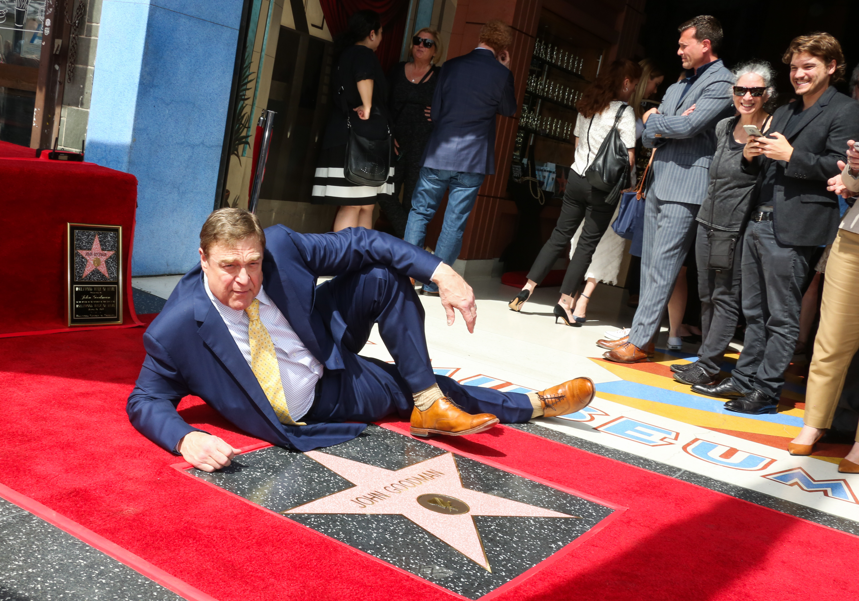 Honored with a star on the Hollywood Walk of Fame in 2017, John Goodman posed playfully on the red carpet in a dark suit and gold tie, resting beside his newly unveiled star.