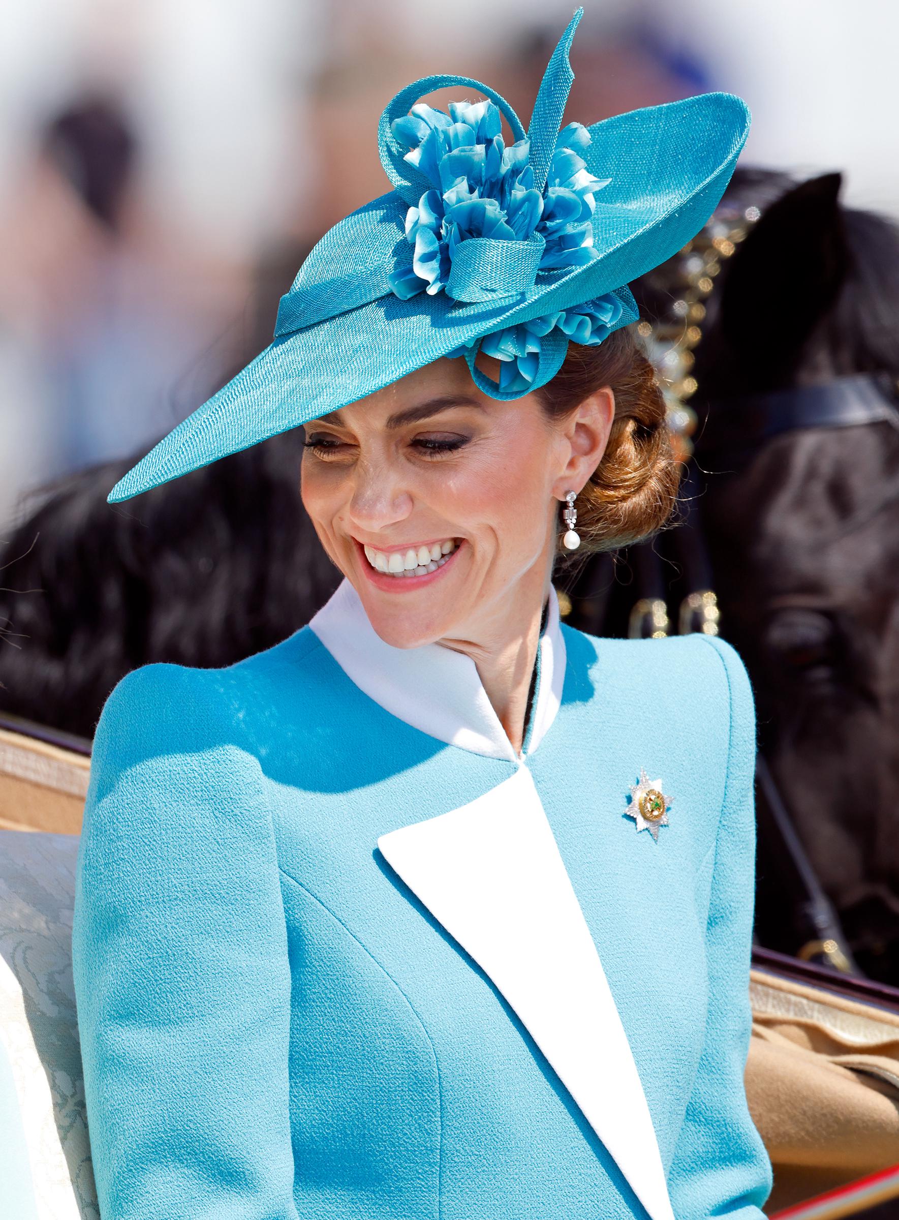 In a close-up captured during her carriage arrival at the 2025 Trooping the Colour, Princess Catherine smiles warmly at the gathered crowd. Her expression radiates calm confidence, framed by the soft floral detailing of her teal hat and the crisp elegance of her ensemble—an image of grace as tradition unfolds.