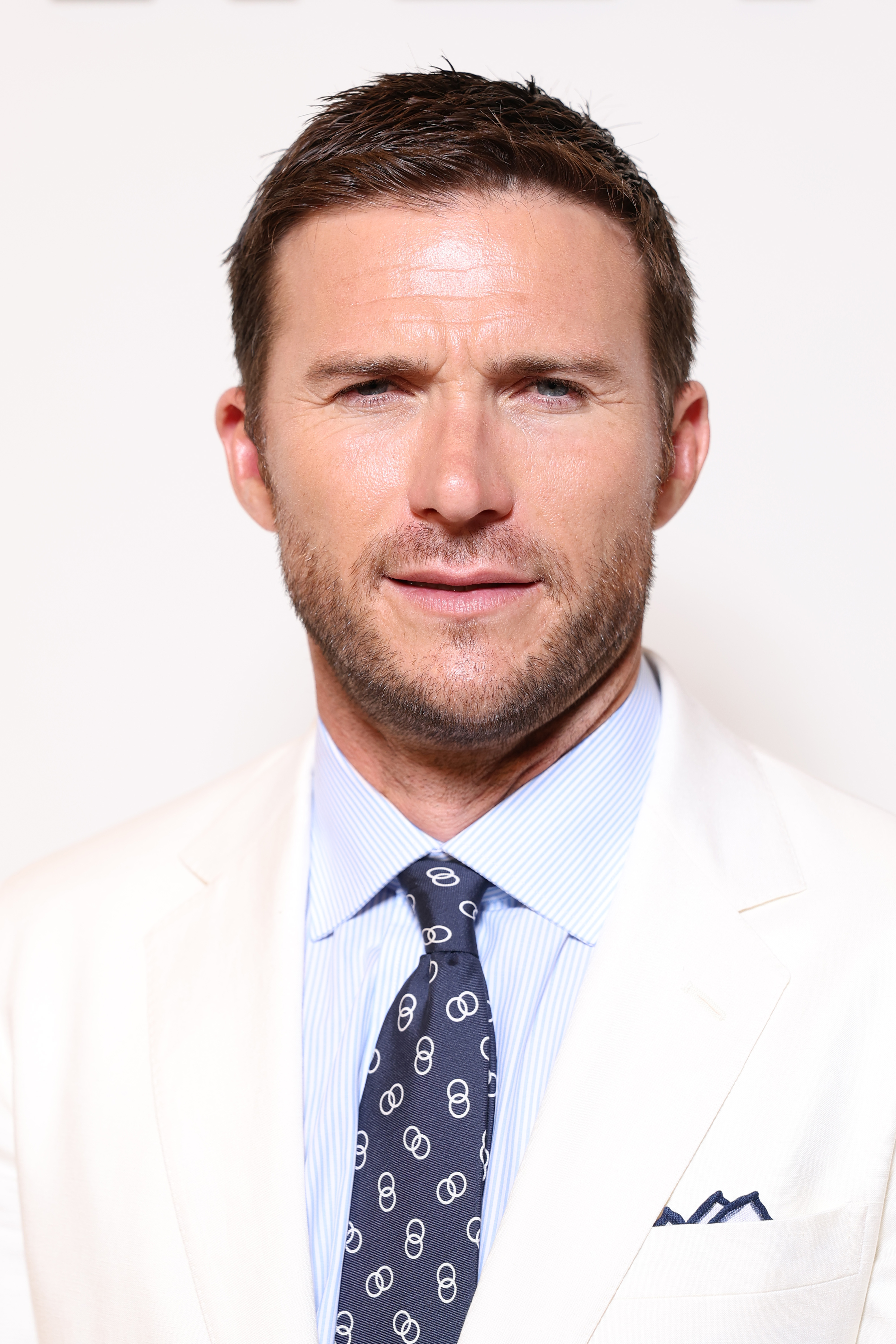 Scott Eastwood attended the Ralph Lauren Spring 2027 Men's Collections Show during Milan Fashion Week in Milan, Italy, on June 19, 2026, arriving in a crisp cream suit layered over a pale blue striped shirt and patterned navy tie. The close-up portrait placed Scott's face squarely in focus, highlighting his blue eyes, lightly furrowed brow, defined jawline, and short brown hair. At 40, the actor's features remained central to the online fascination surrounding his appearance, with netizens singling out his "stormy eyes."