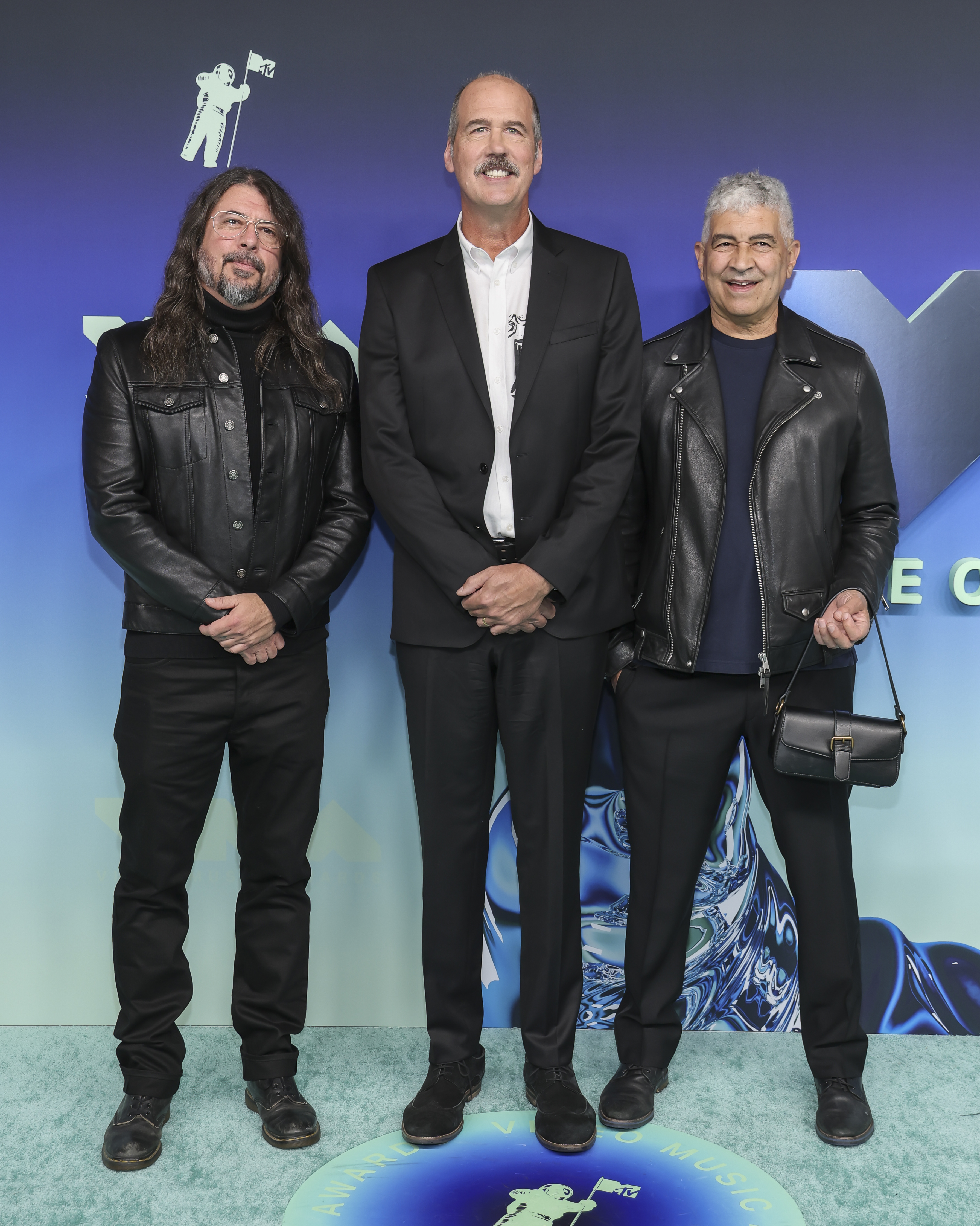 Grohl, Novoselic, and Smear posed together in a coordinated dark palette, with leather jackets flanking Novoselic's black suit and white shirt. The trio kept their VMAs styling rooted in black tailoring and rock staples. | Source: Getty Images