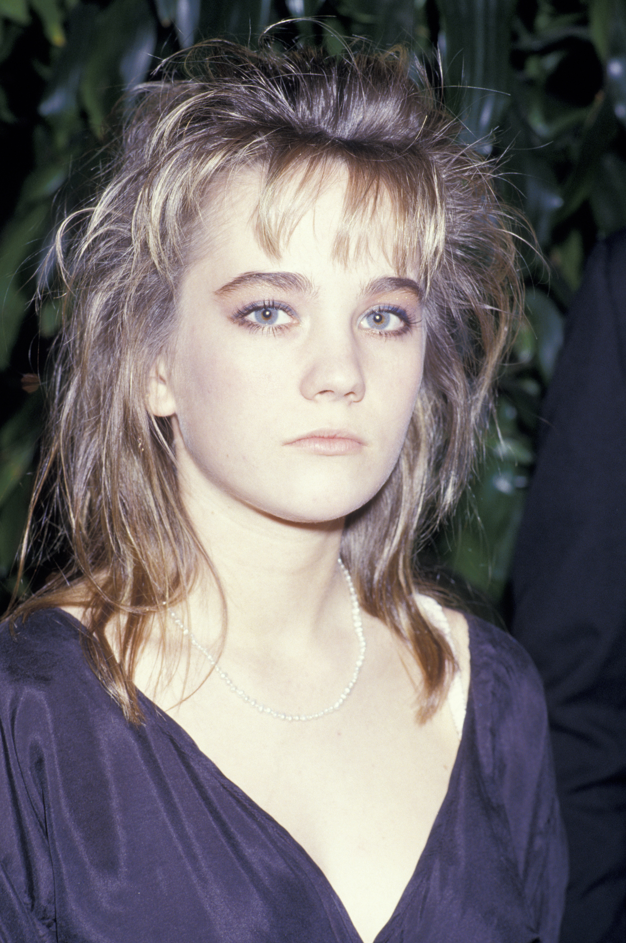 Natasha Gregson Wagner attends the 4th Annual American Cinema Awards at the Beverly Wilshire Hotel in January 1987. She wears a deep purple dress with a pearl necklace, her hair styled in a tousled, voluminous look.