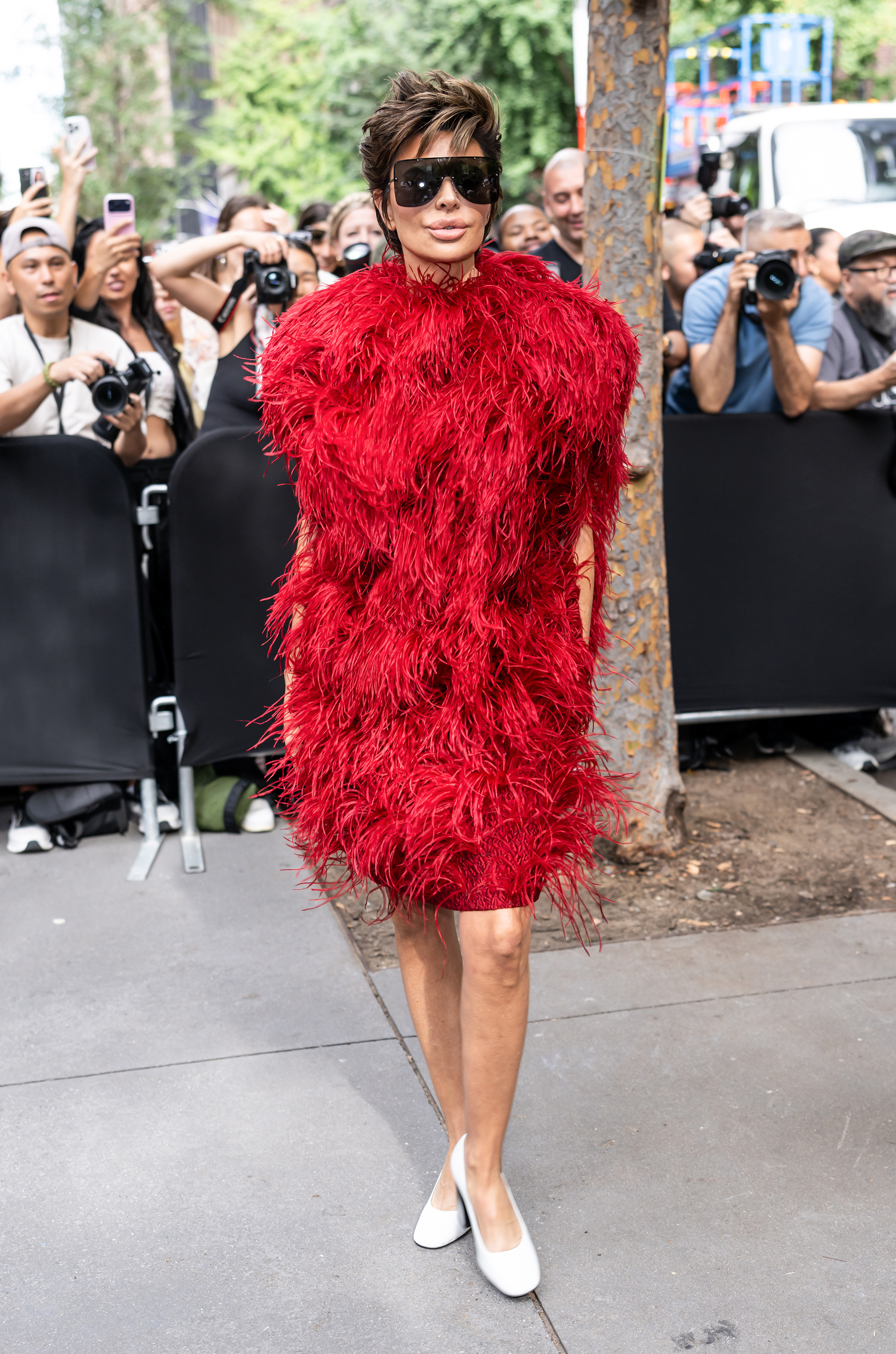 Lisa Rinna steps out in a vibrant red feathered dress, oversized black sunglasses, and white pumps as photographers and fans gather around her. Her signature short, tousled hairstyle complements the dramatic look, reflecting her love of bold fashion statements. | Source: Getty Images.