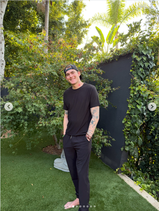 Presley Gerber tilts his head and smiles broadly at the camera, posing barefoot with his hands in his pockets as he stands among the lush greenery. | Source: Instagram/presleygerber