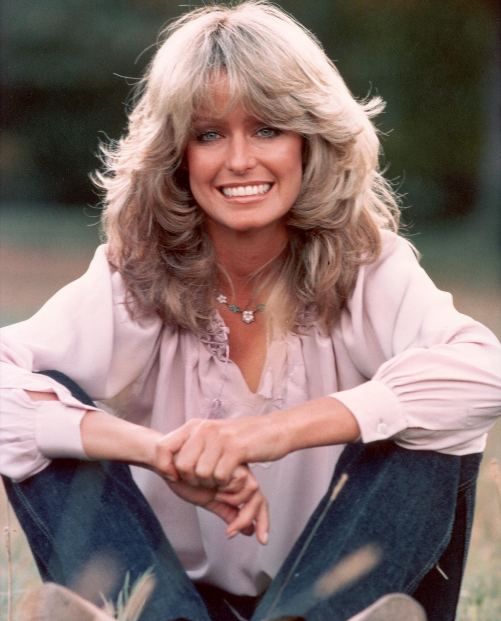 Publicity portrait of Farrah Fawcett smiling while sitting outdoors in blue jeans and a mauve blouse, taken in 1975. | Source: Getty Images