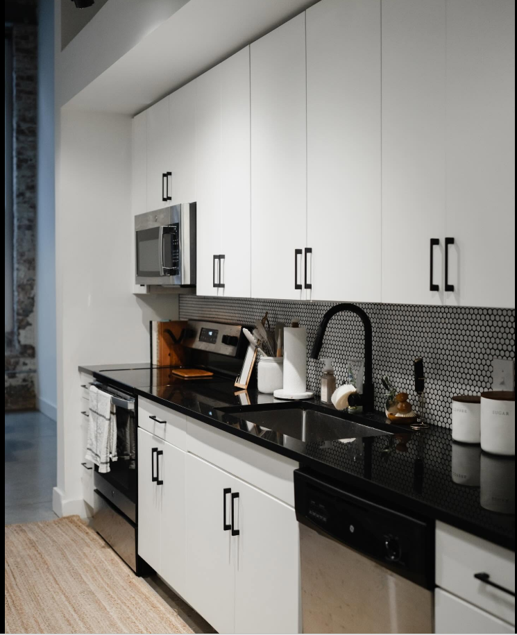 The kitchen continues the loft’s modern-industrial look, pairing crisp white cabinetry with black countertops, stainless-steel appliances and a textured backsplash. | Source: Facebook/Judson Mills Loft