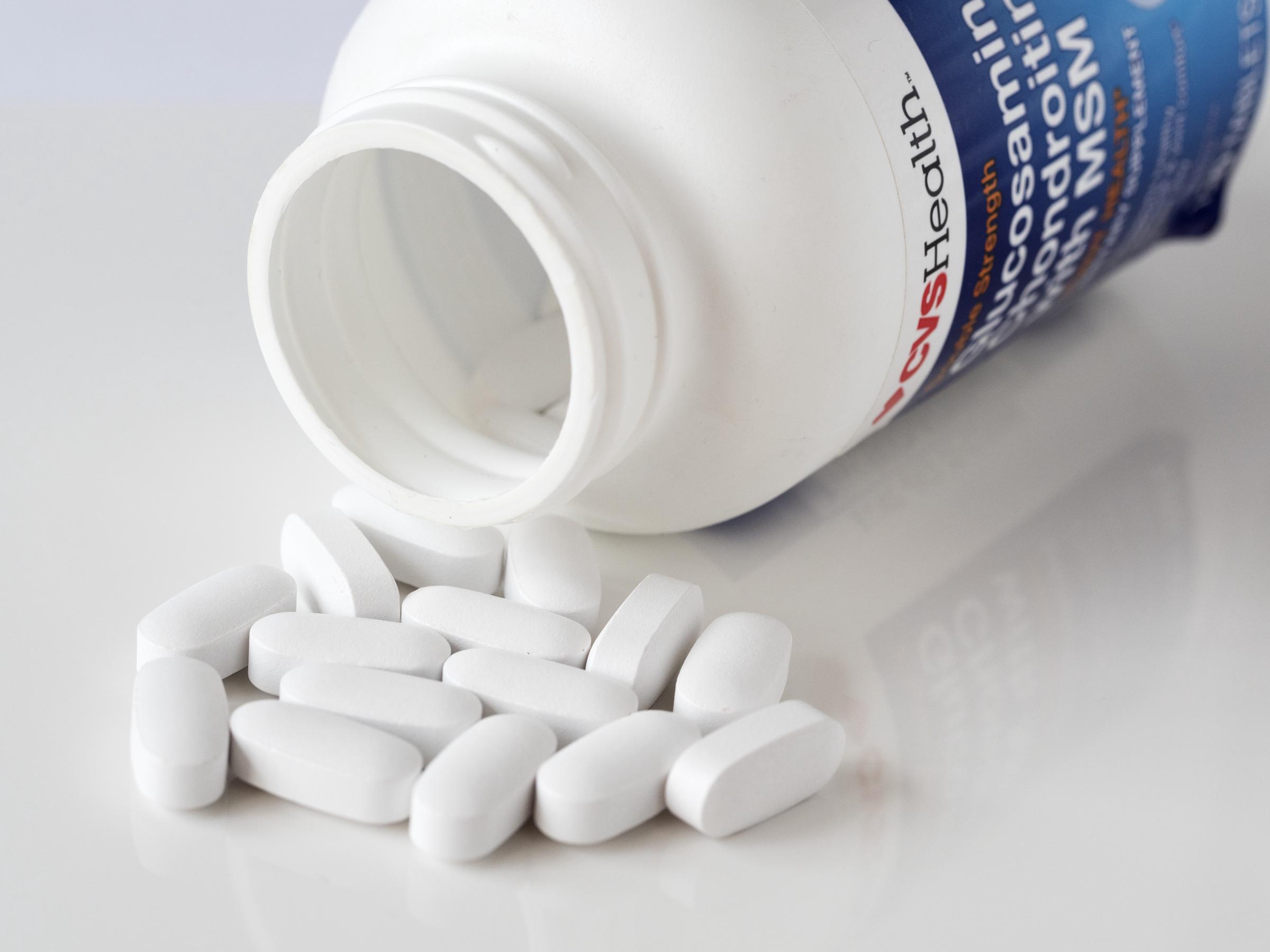 White oblong caplets spill out across a reflective white surface from an open pill bottle in a studio photo illustration captured on July 19, 2019. | Source: Getty Images