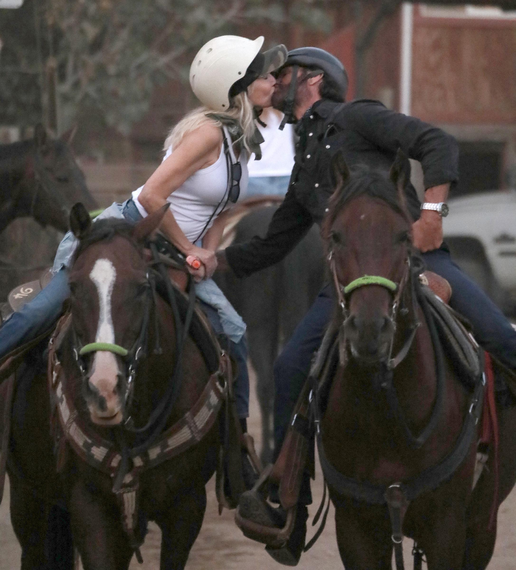 Heather Locklear and Lorenzo Lamas share a sweet kiss from atop their horses during a visit to Sunset Ranch in the Hollywood Hills on September 22, 2026, in Los Angeles, California. Dressed for horseback riding in protective riding helmets and denim jeans, Locklear wears a white tank top while leaning in to kiss Lamas, who sports a black button-down shirt and wristwatch. | Source: Getty Images